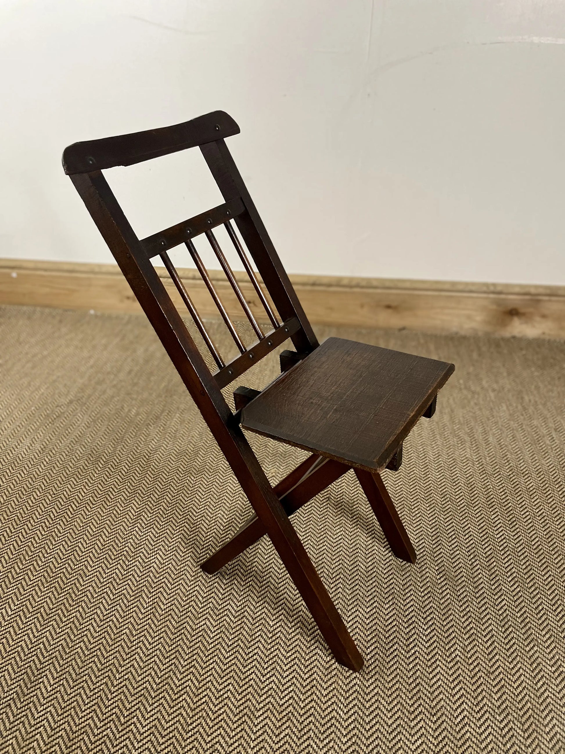 An antique oak folding child's chair with a dark finish, featuring a straight back and seat, with intricate slat detailing.