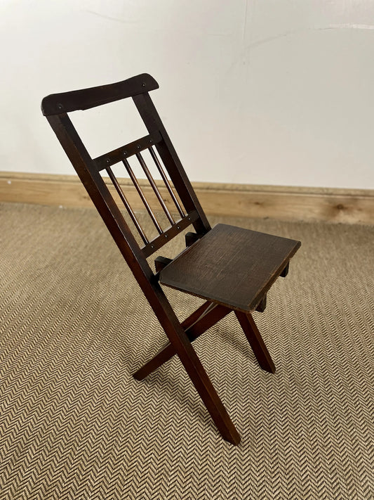 An antique oak folding child's chair with a dark finish, featuring a straight back and seat, with intricate slat detailing.
