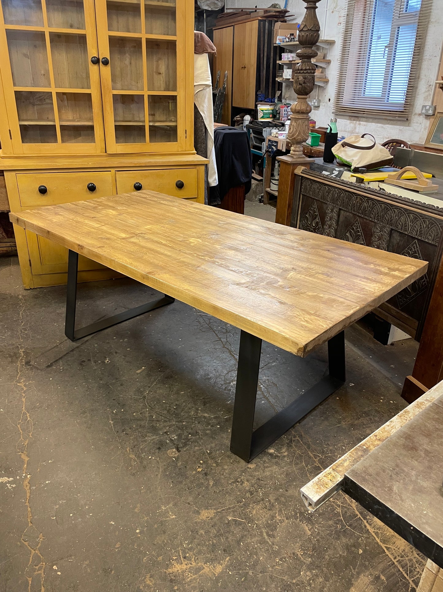 A large rectangular pine wood dining table with a metal base, designed to seat 10 people, in a room with various furniture.