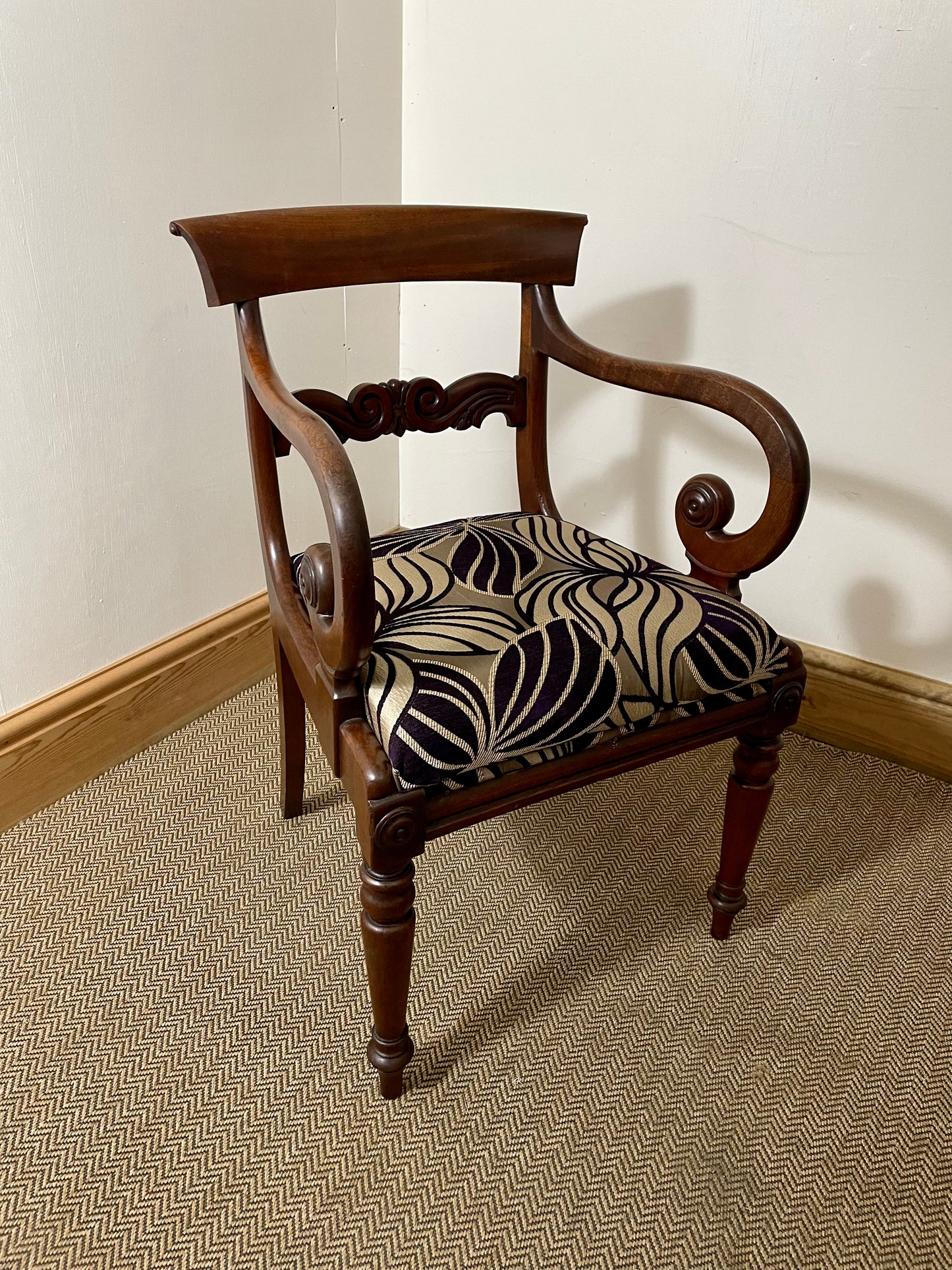 A Victorian Antique Scroll Arm Chair with a wooden frame and a patterned fabric seat cushion.