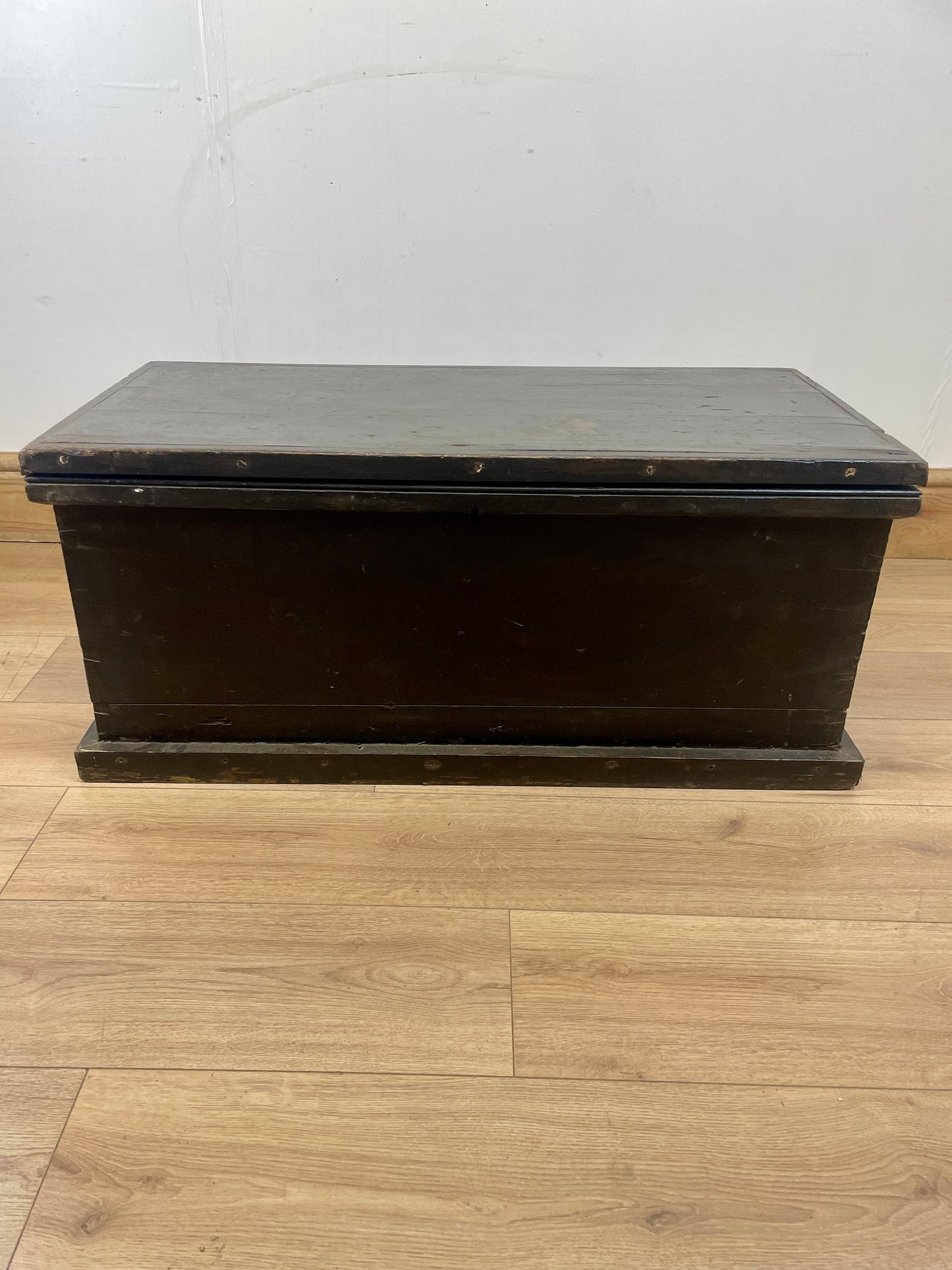 Dark wooden box on a light wood floor with a white wall background