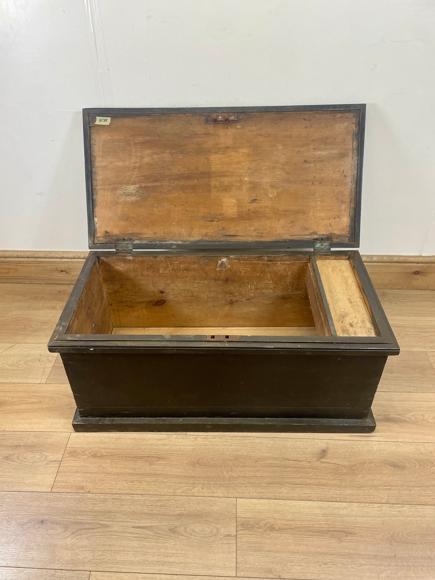 Wooden trunk with open lid on a wooden floor against a white wall