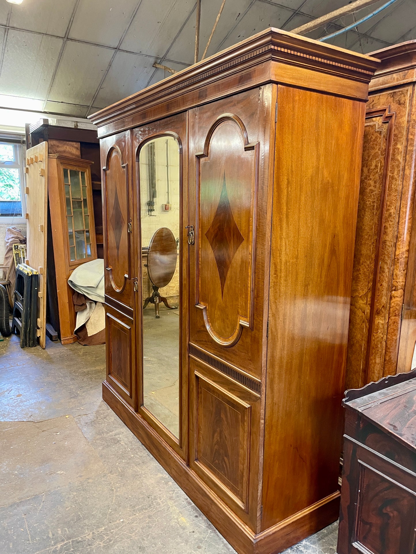 Large wooden wardrobe with mirrored doors in a storage or warehouse setting.