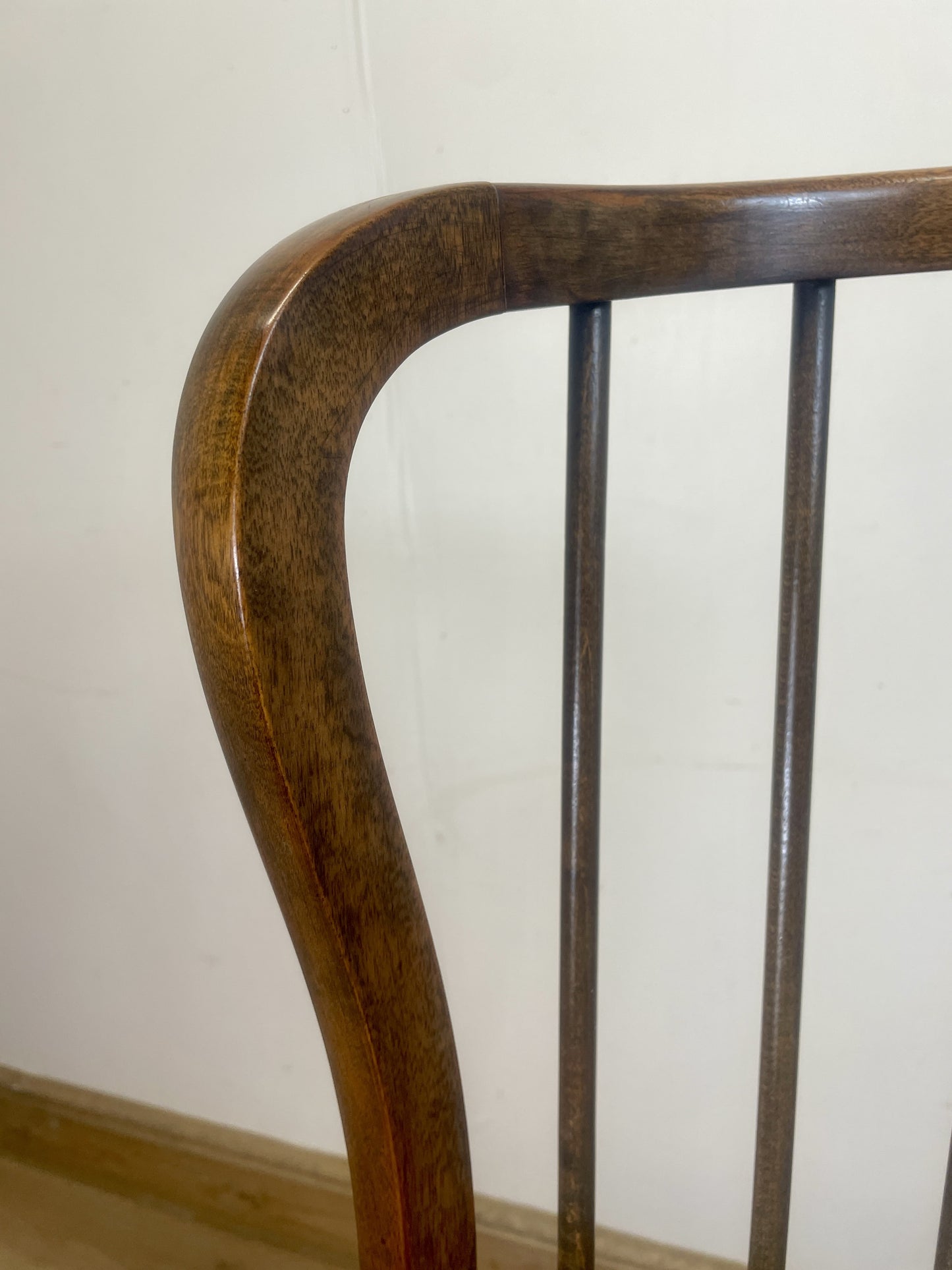 Close-up of a wooden chair backrest against a white wall.