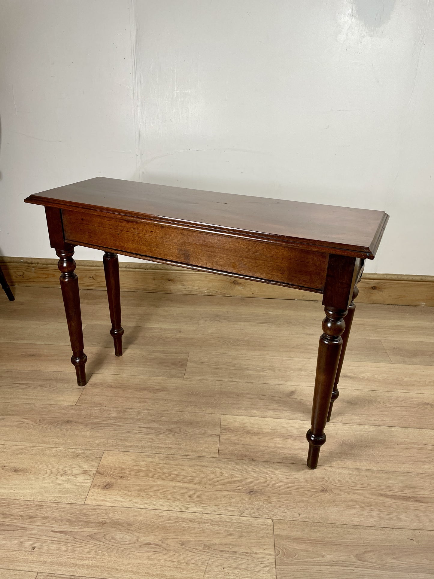 Wooden table with a dark finish on a wooden floor against a white wall