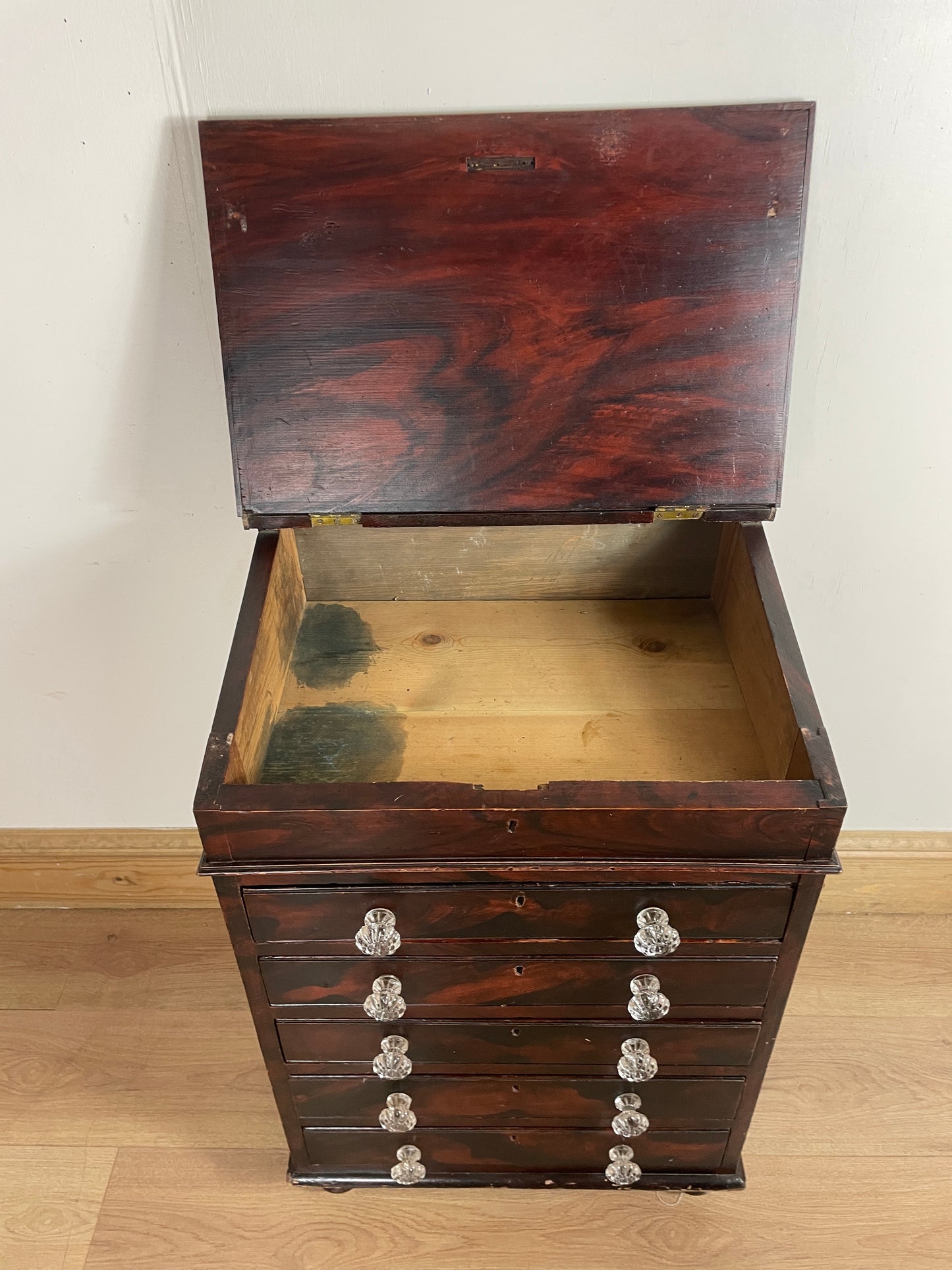 Wooden box with a textured surface, open to reveal greenery inside, on a light wooden floor.