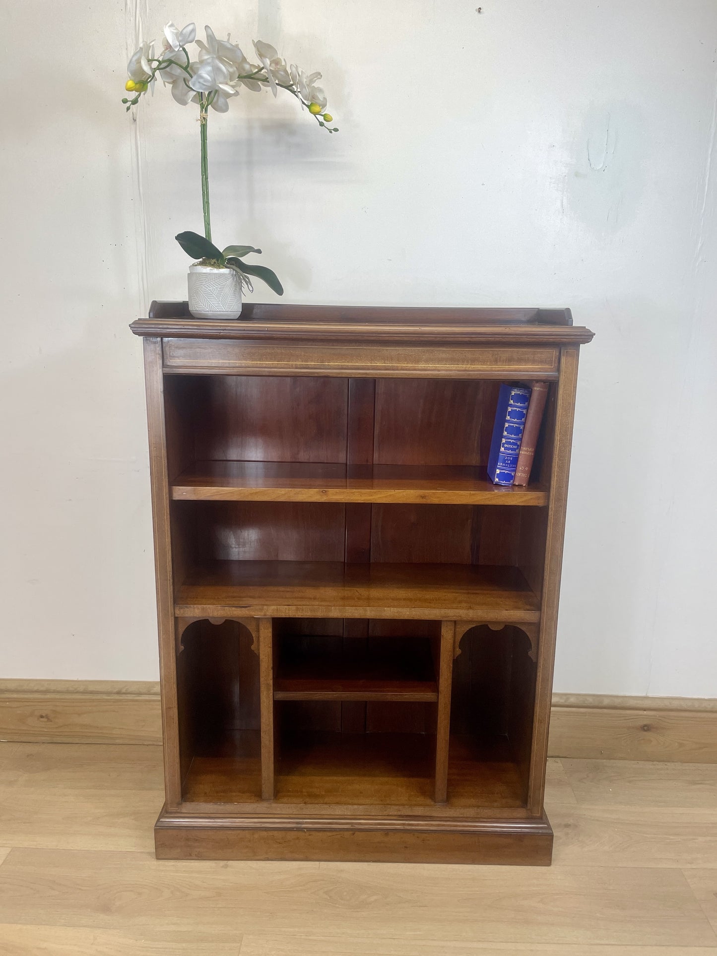 Wooden bookshelf with a vase of flowers on top against a white wall.