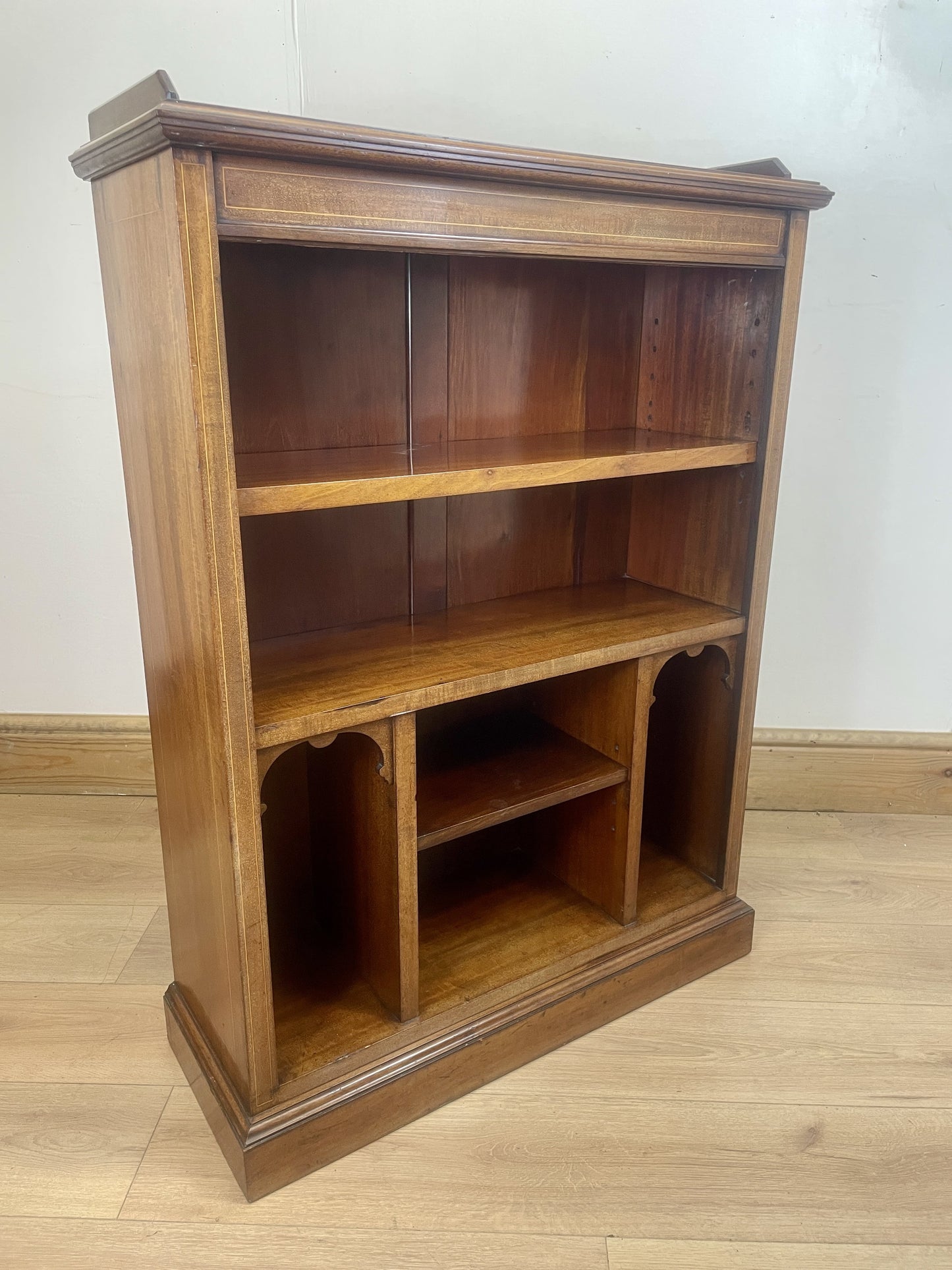 Wooden bookshelf with three shelves on a wooden floor against a white wall