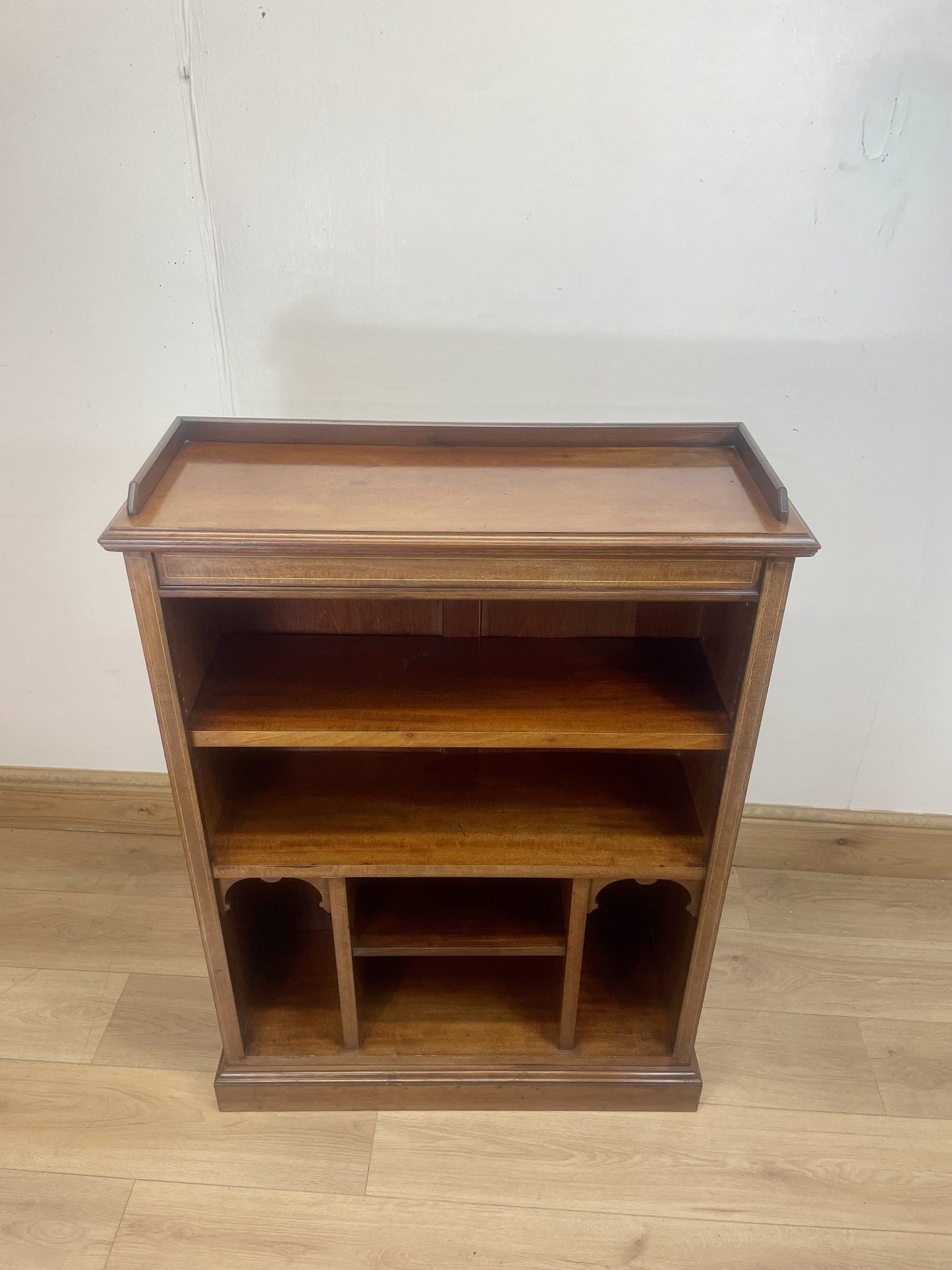 Wooden bookshelf with three shelves on a wooden floor against a white wall