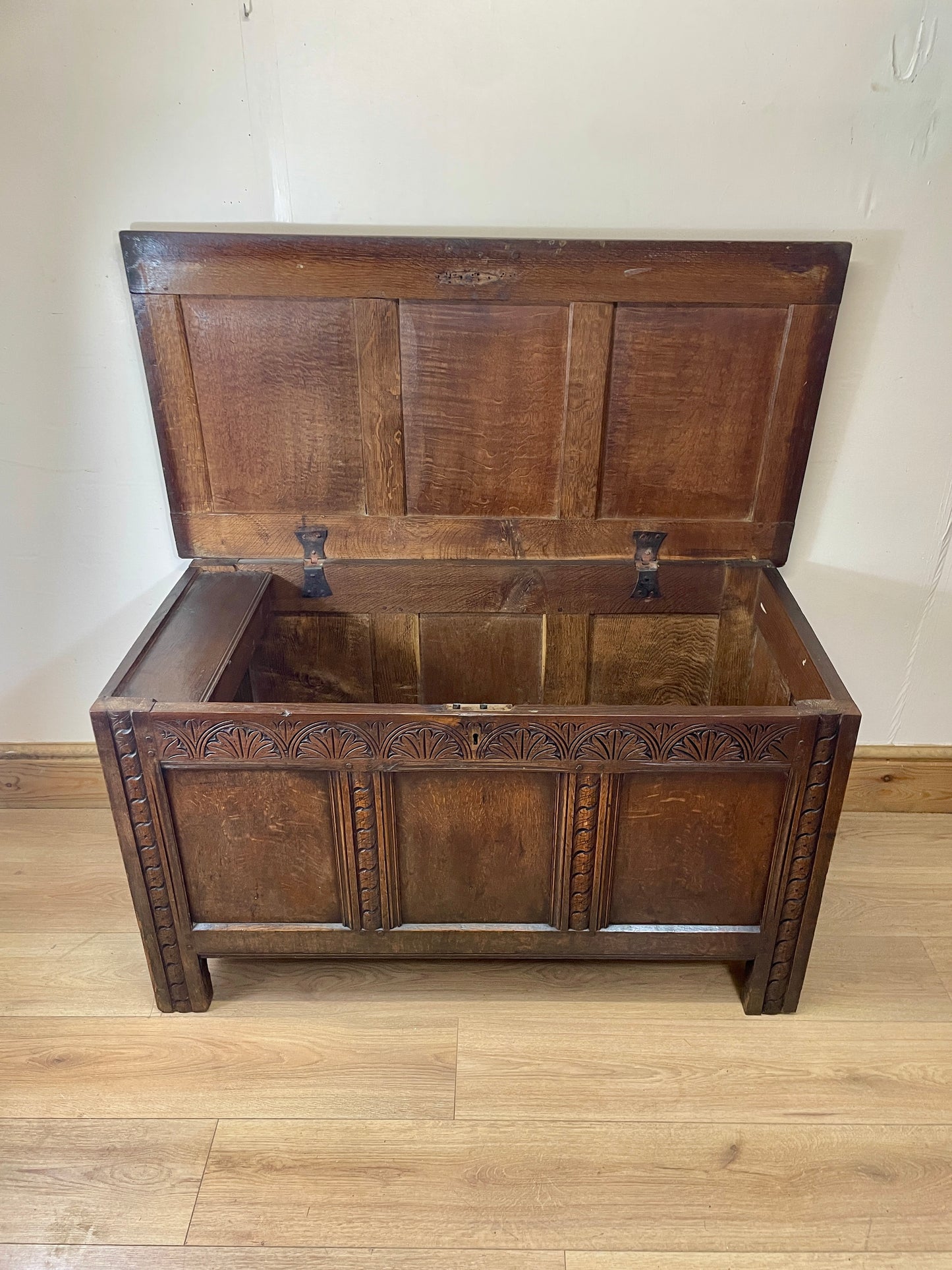 Wooden chest with a hinged lid on a wooden floor against a white wall