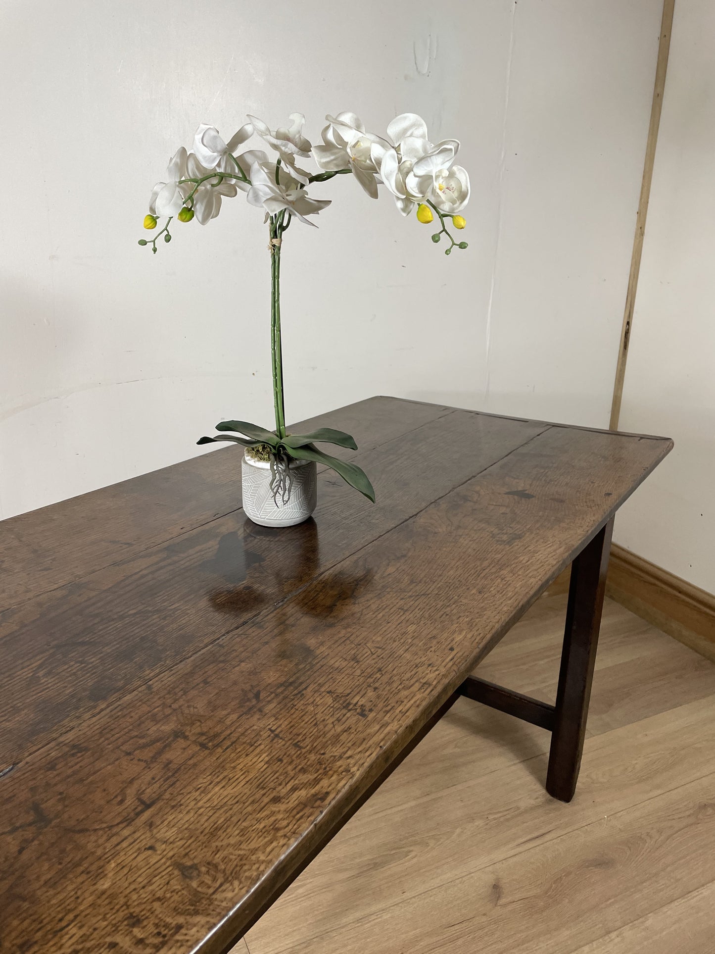 Floral arrangement in a pot on a wooden table against a plain wall.