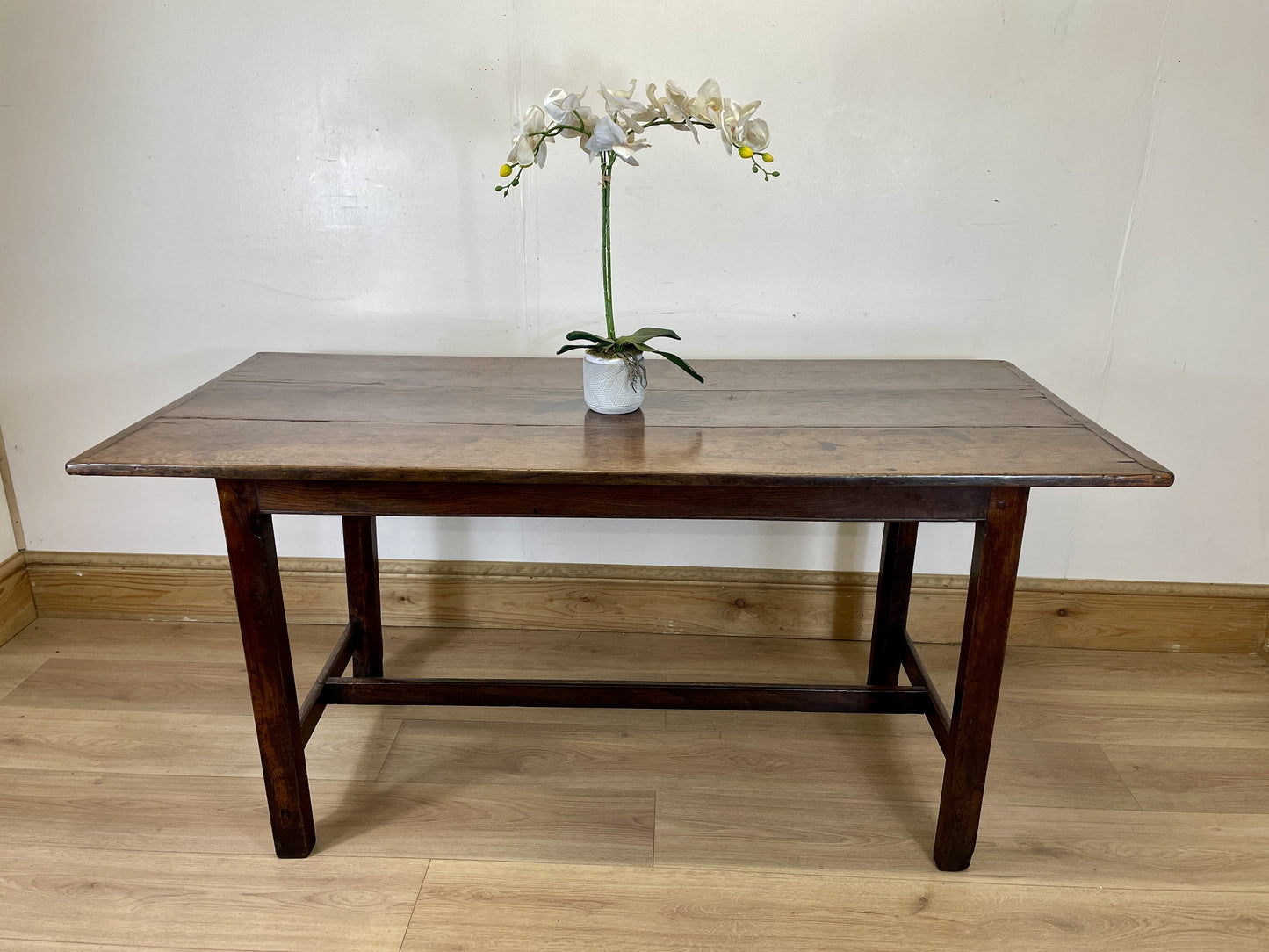 Wooden table with a vase of flowers on a wooden floor against a white wall