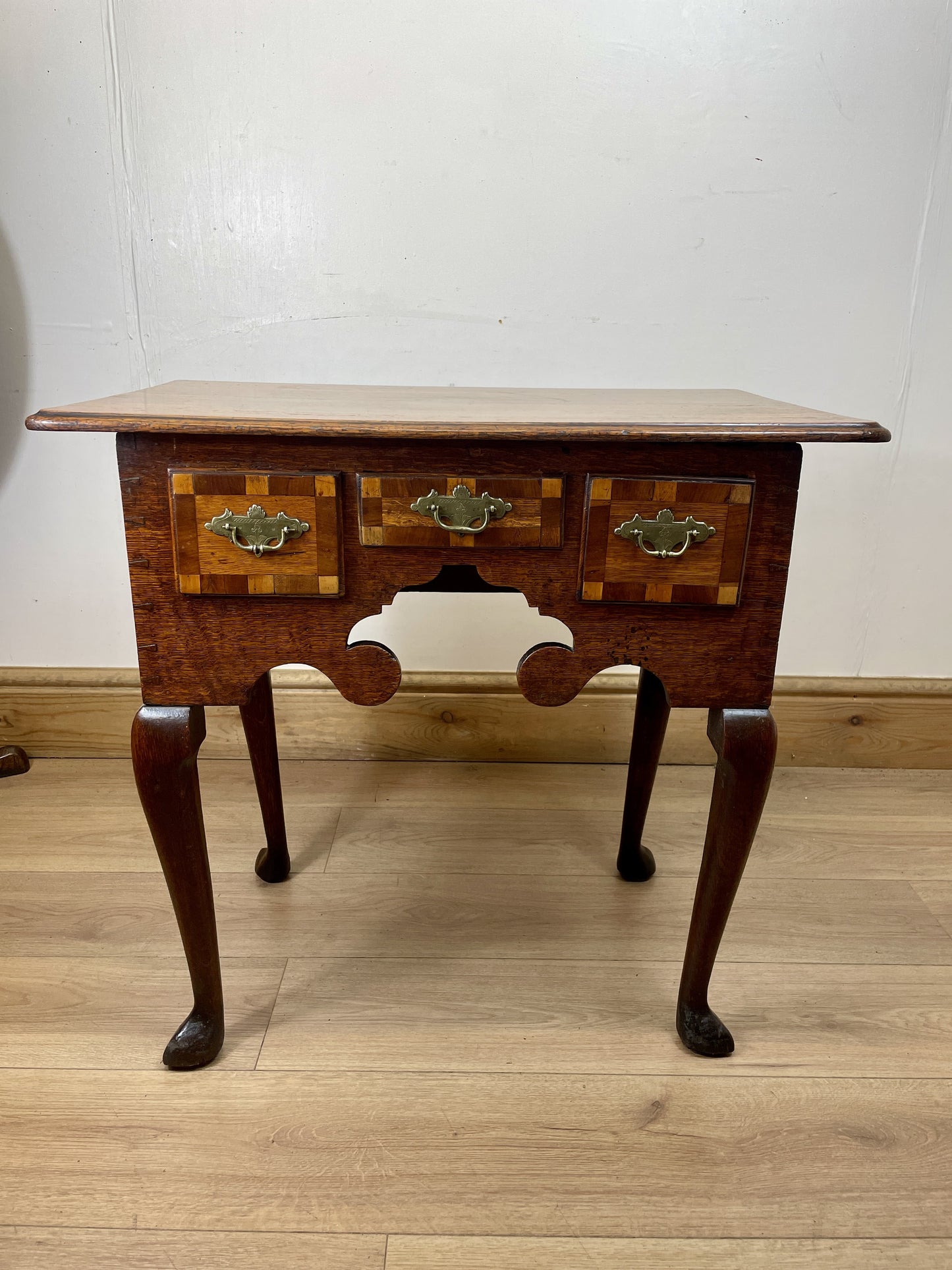 Wooden side table with inlaid design on a wooden floor against a white wall