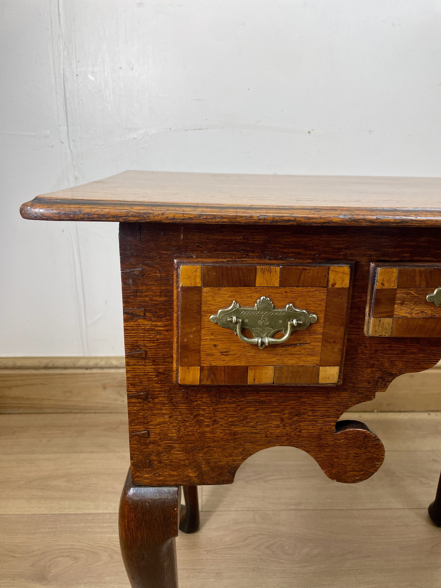 Wooden side table with a checkered pattern and brass handle on a wooden floor.