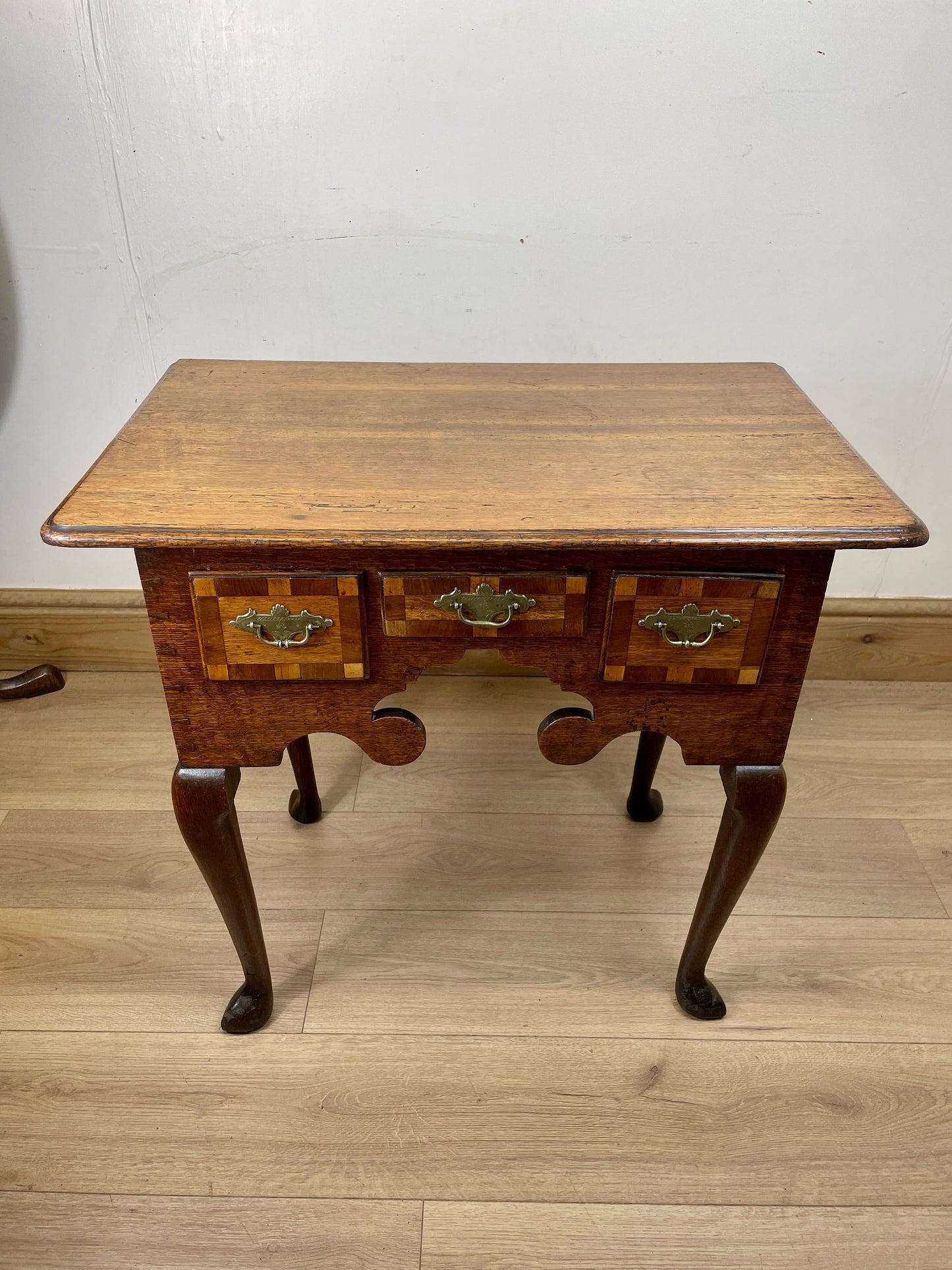 Wooden side table with two drawers on a wooden floor against a white wall