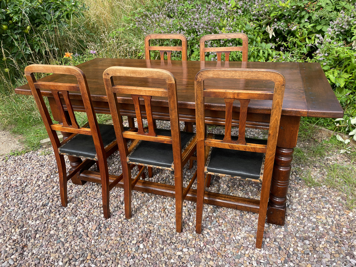 Wooden dining table with six matching chairs outdoors on a gravel surface.