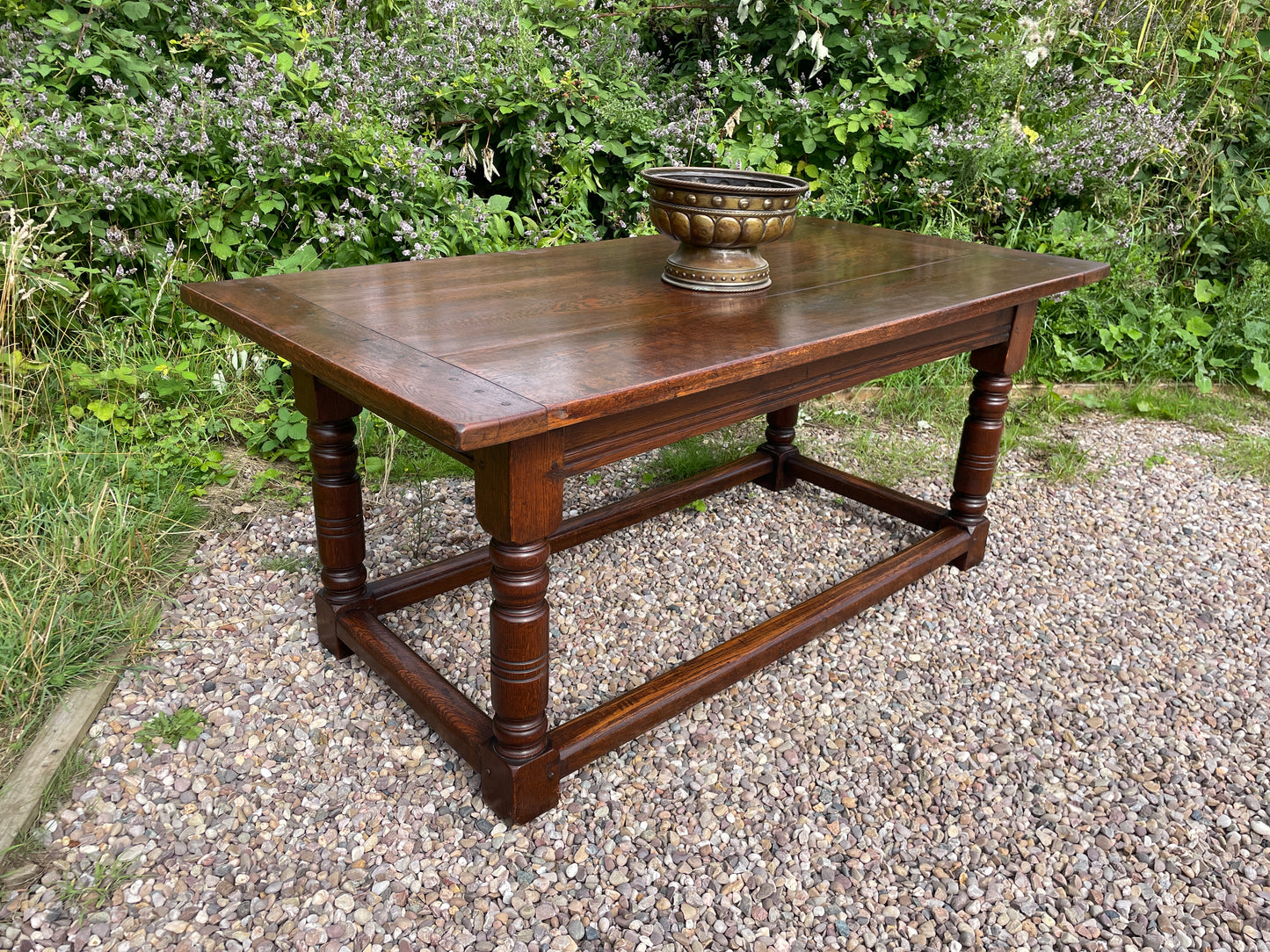 Wooden table with a decorative bowl on a gravel surface with greenery in the background