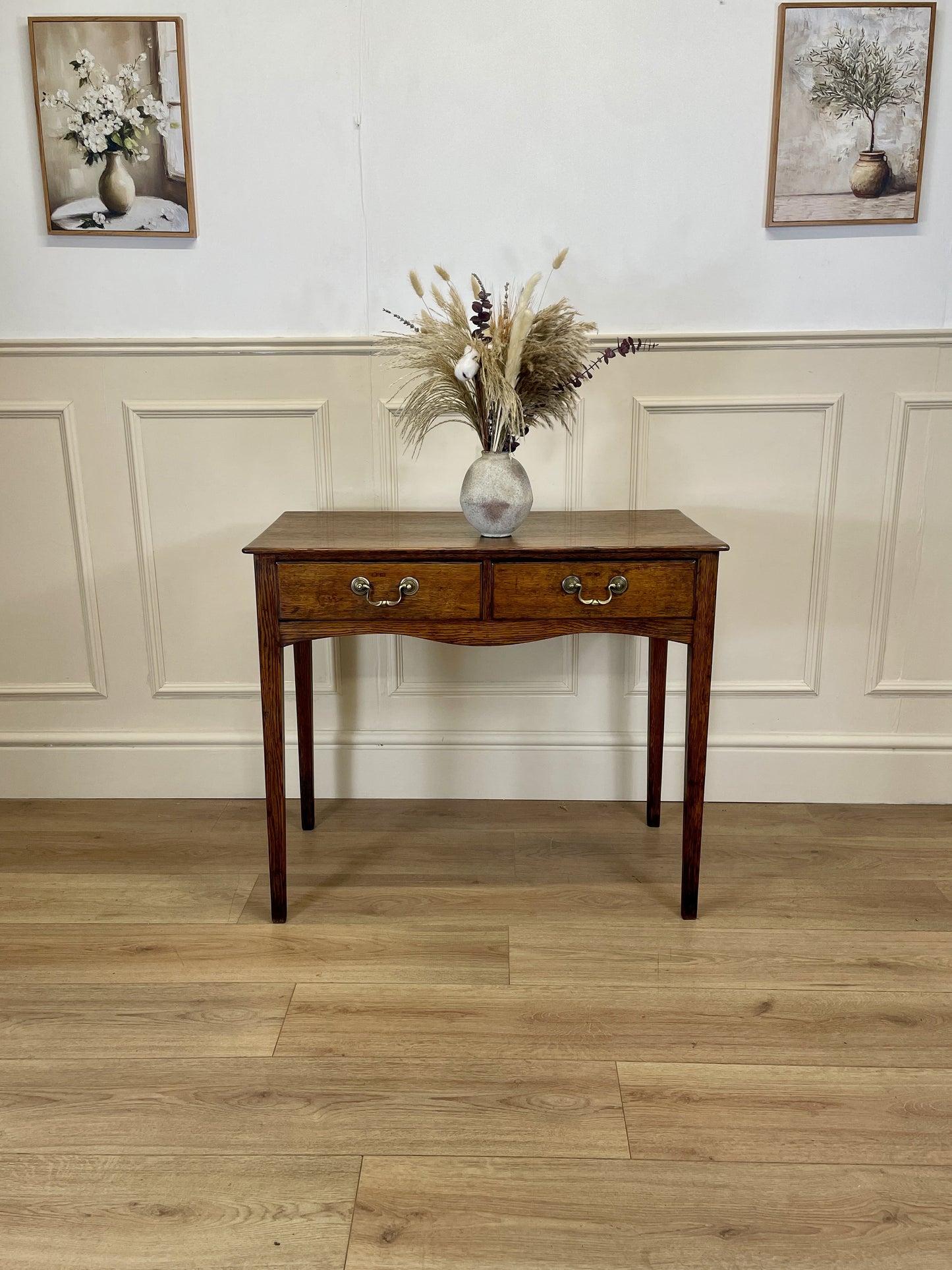 Wooden console table with a vase of flowers on a wooden floor with white walls.