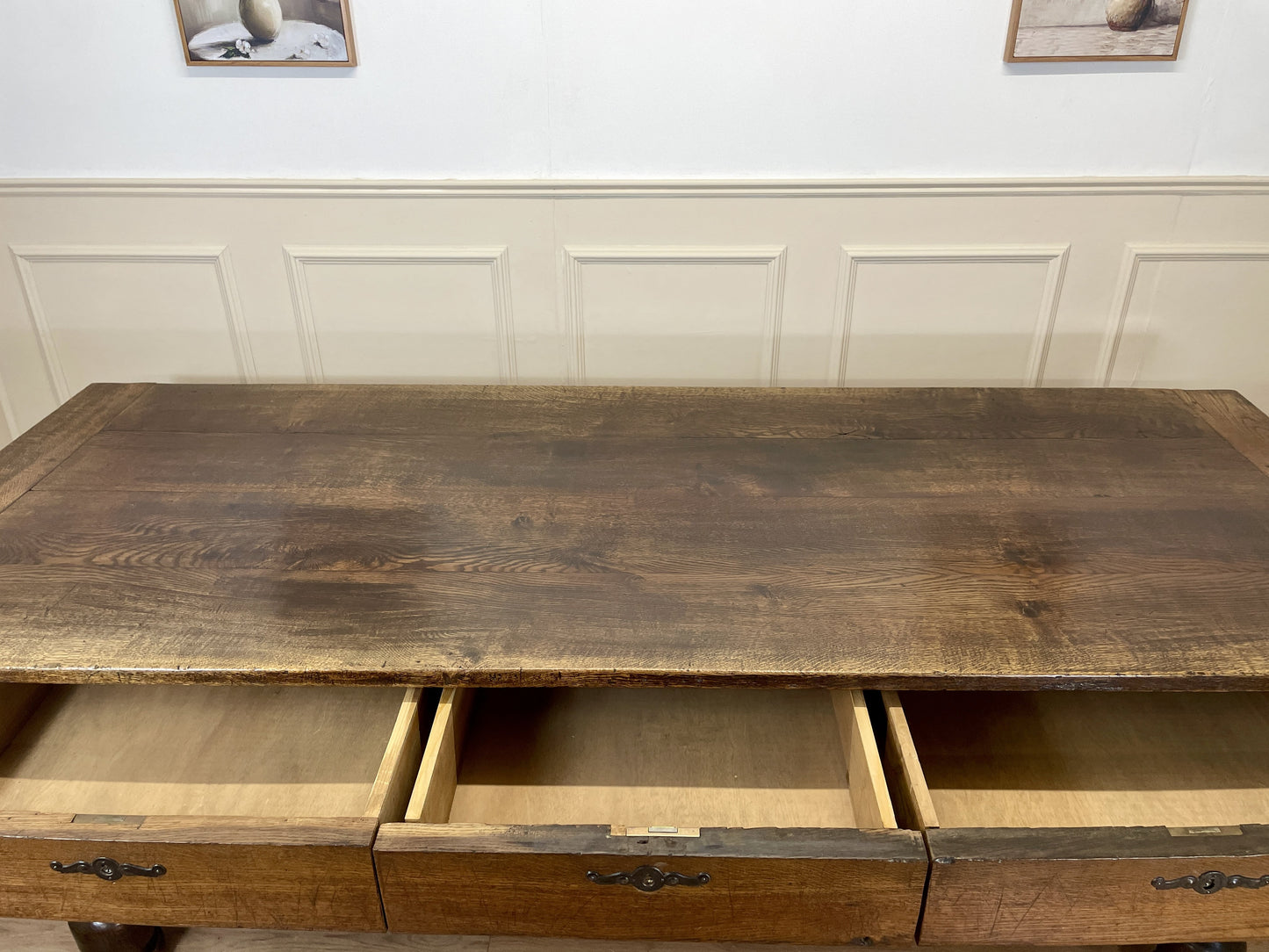 Wooden desk with drawers against a white paneled wall.