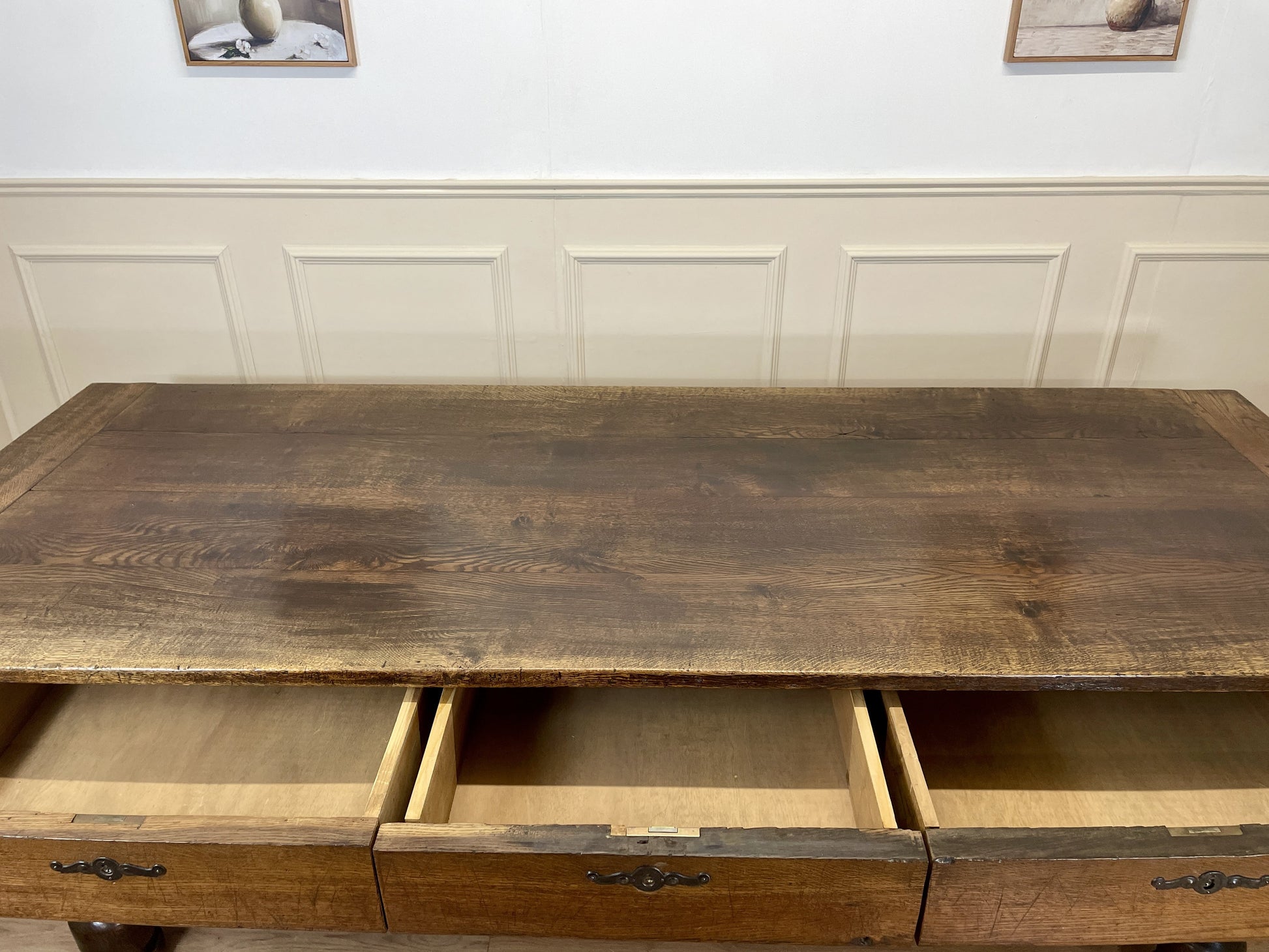 Wooden desk with drawers against a white paneled wall.
