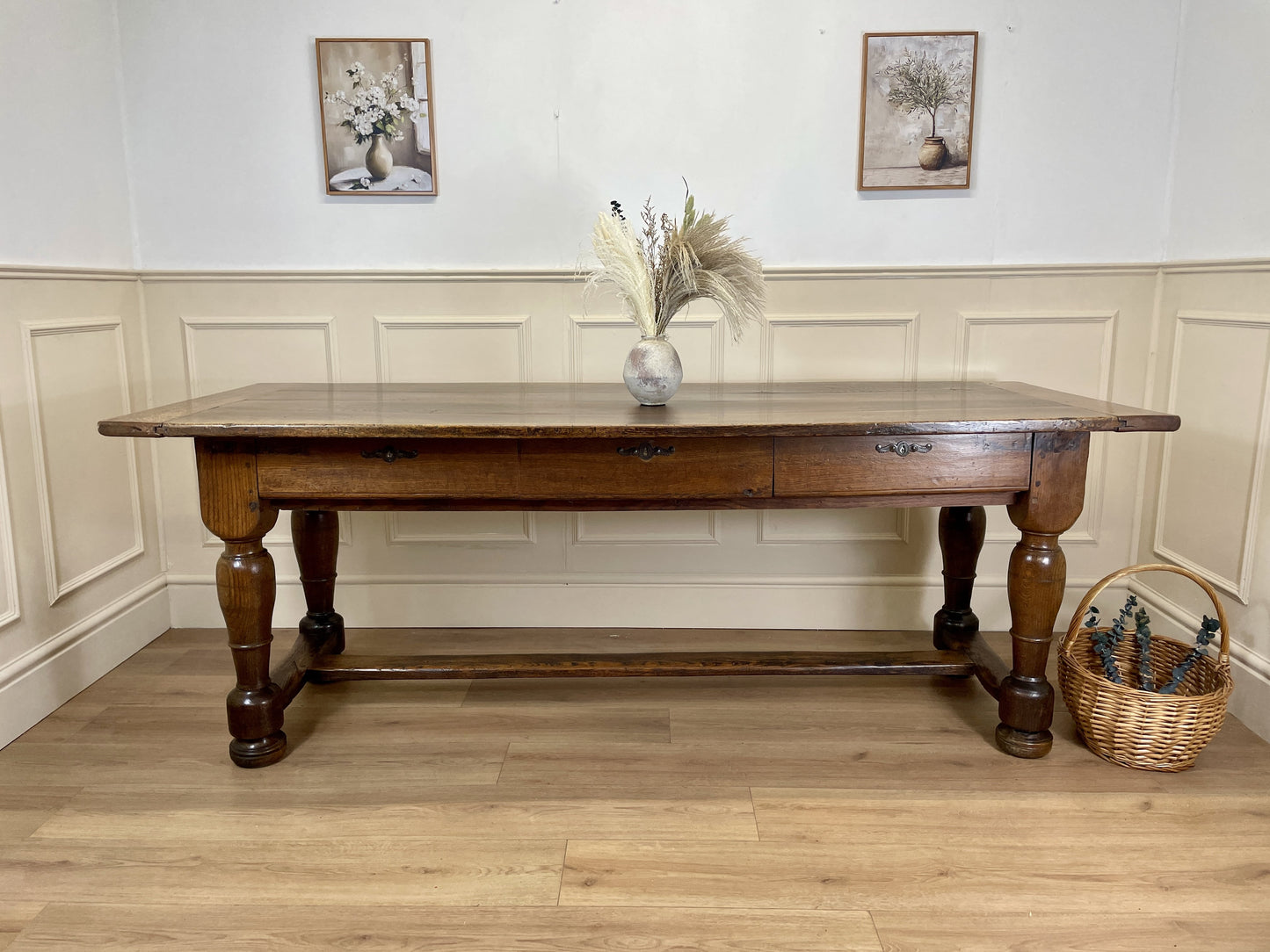 Wooden dining table with a shelf against a white paneled wall.