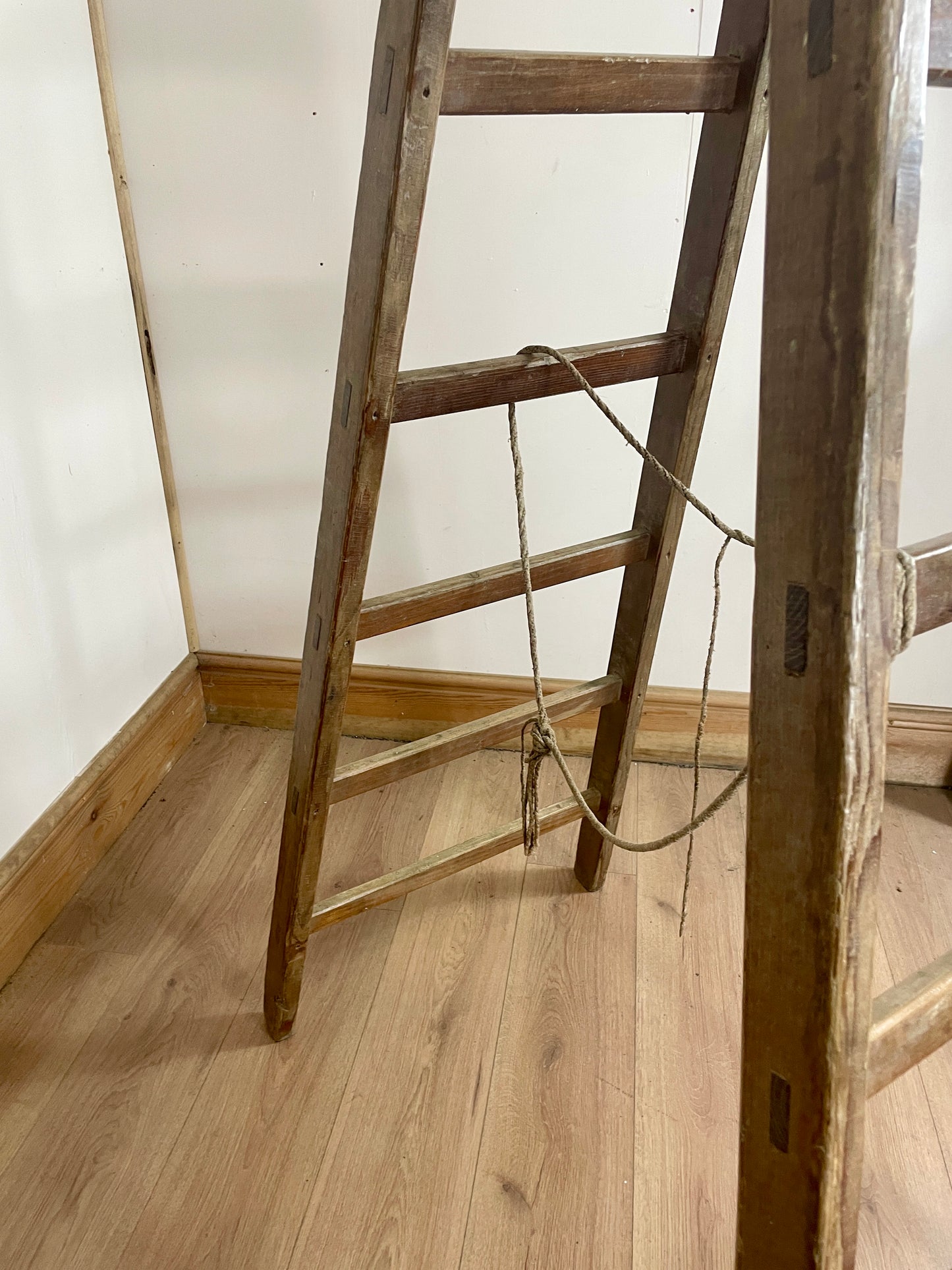 Wooden ladder leaning against a wall in a room with wooden flooring.