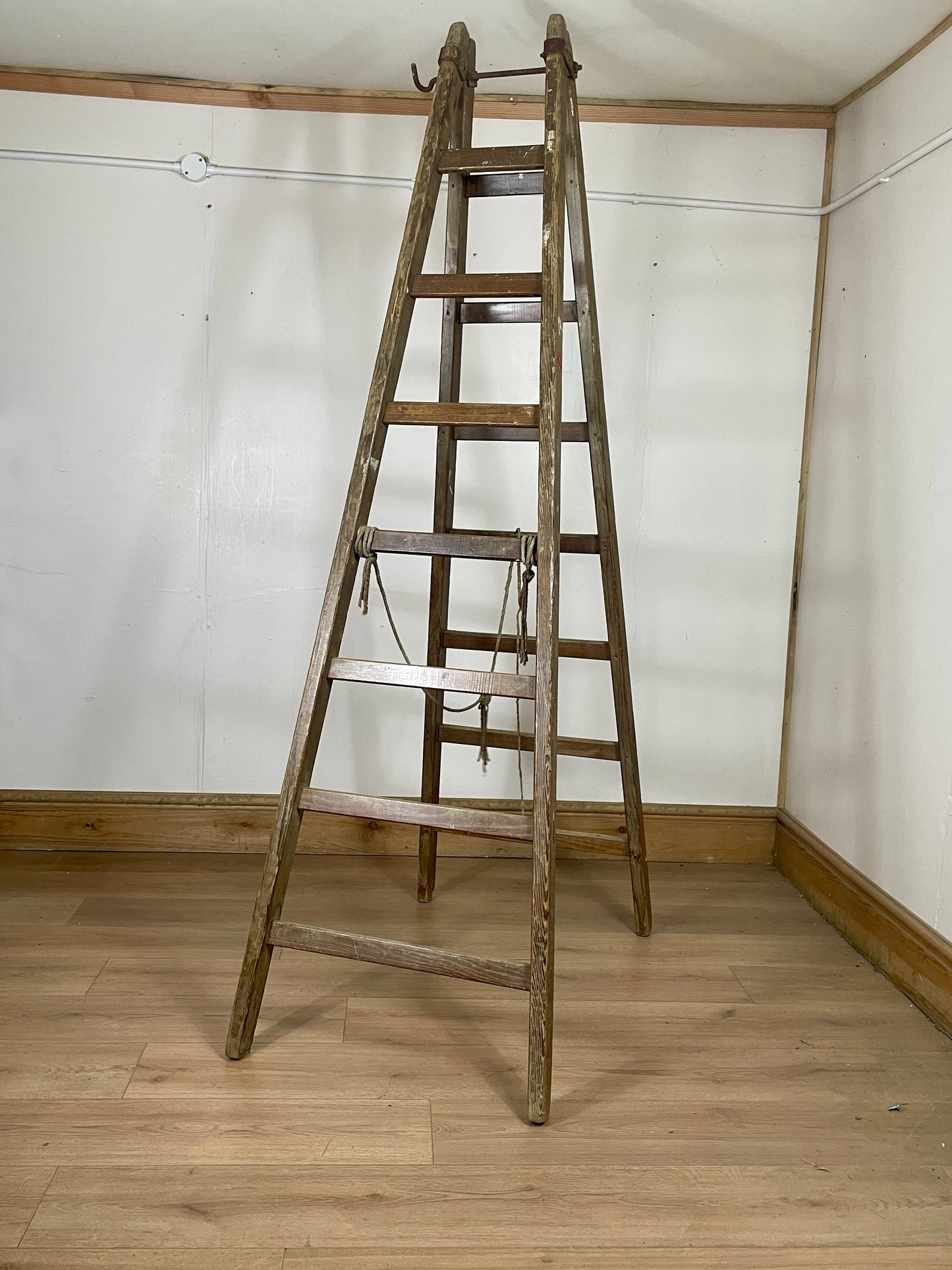 Wooden ladder leaning against a white wall in a room with wooden floor.