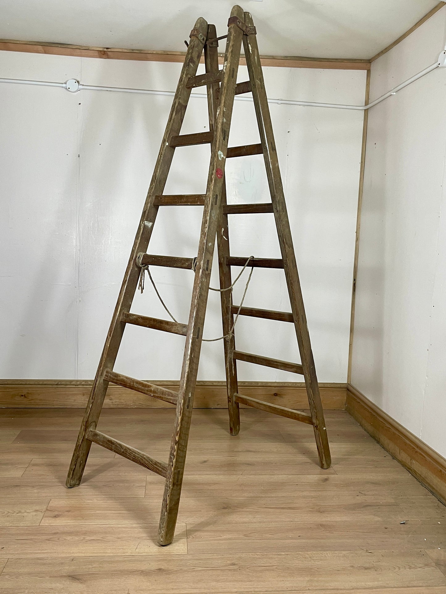 Wooden ladder leaning against a white wall in a room with wooden floor.