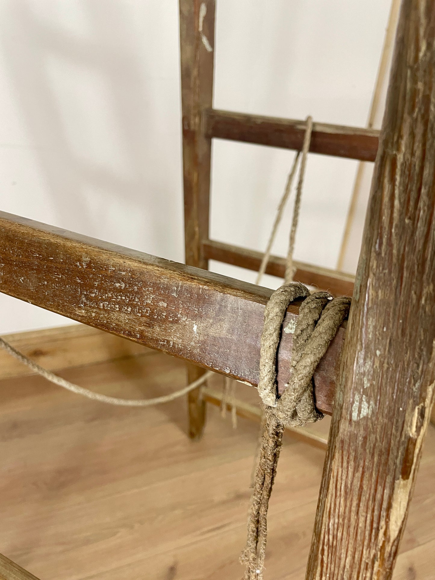 Wooden ladder with a rope tied to it on a wooden floor.