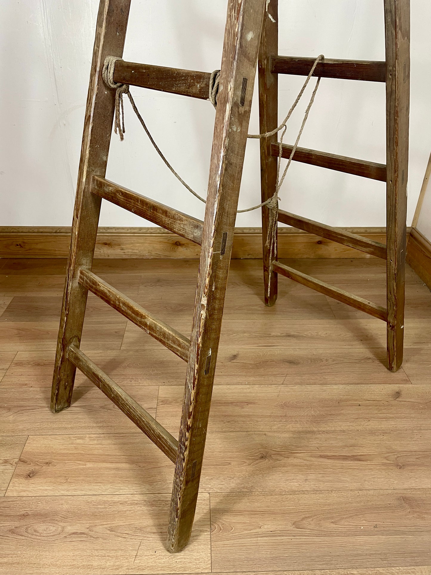 Wooden ladders leaning against a white wall on a wooden floor.