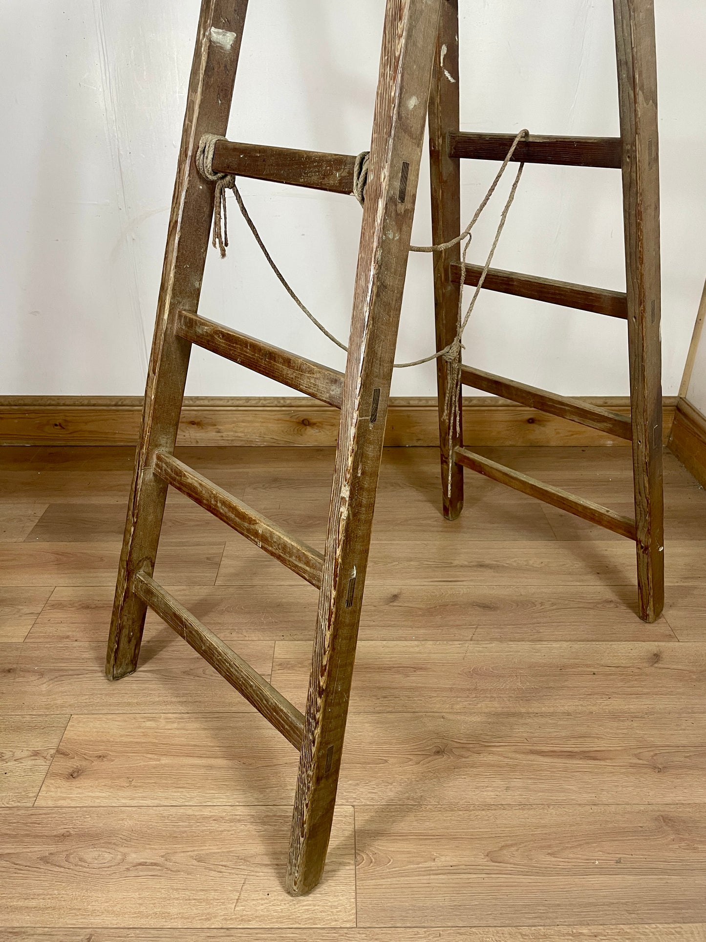 Old wooden ladder leaning against a white wall on a wooden floor