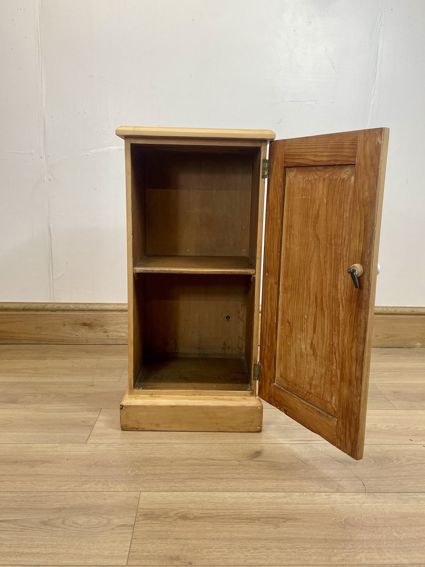 Wooden cabinet with an open door on a wooden floor against a white wall