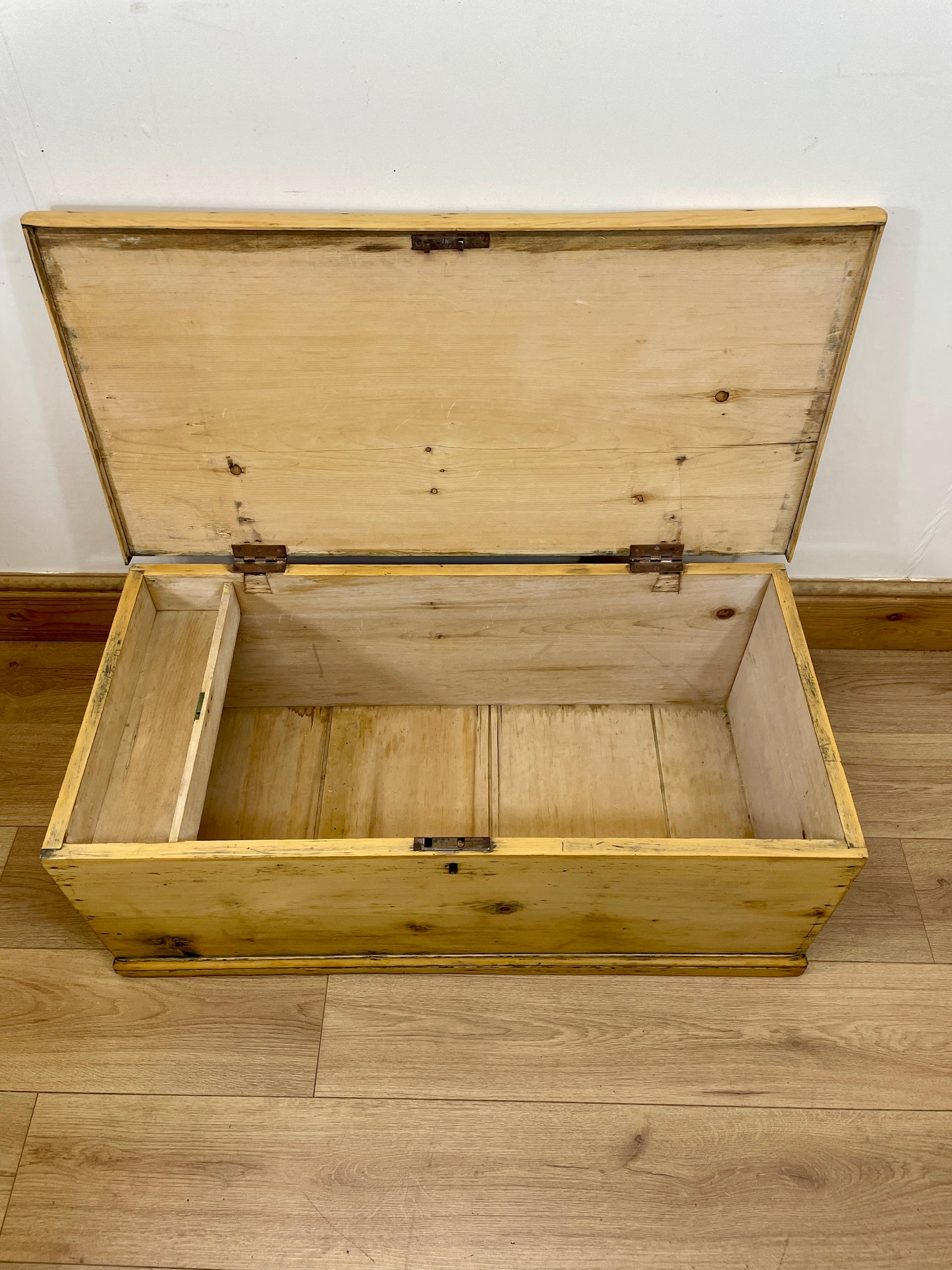 Wooden storage chest with a lid open on a wooden floor.