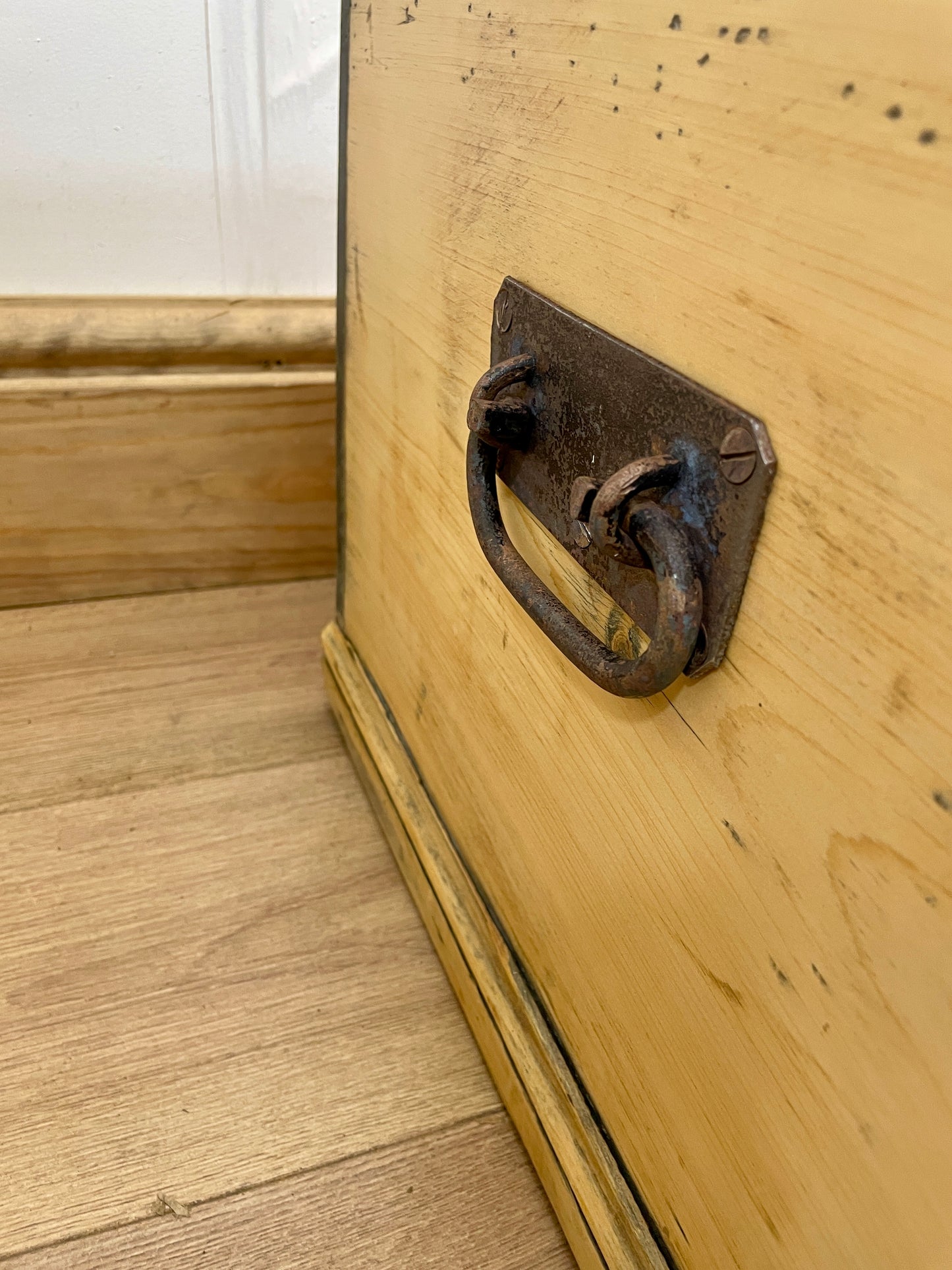 Close-up of a wooden trunk with a metal handle on a wooden floor.