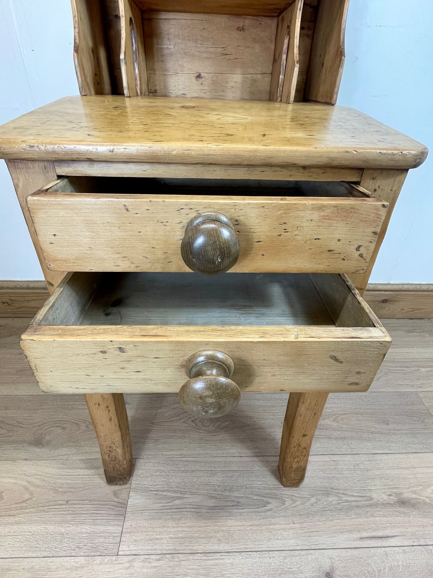Wooden side table with two drawers and metal knobs on a wooden floor.