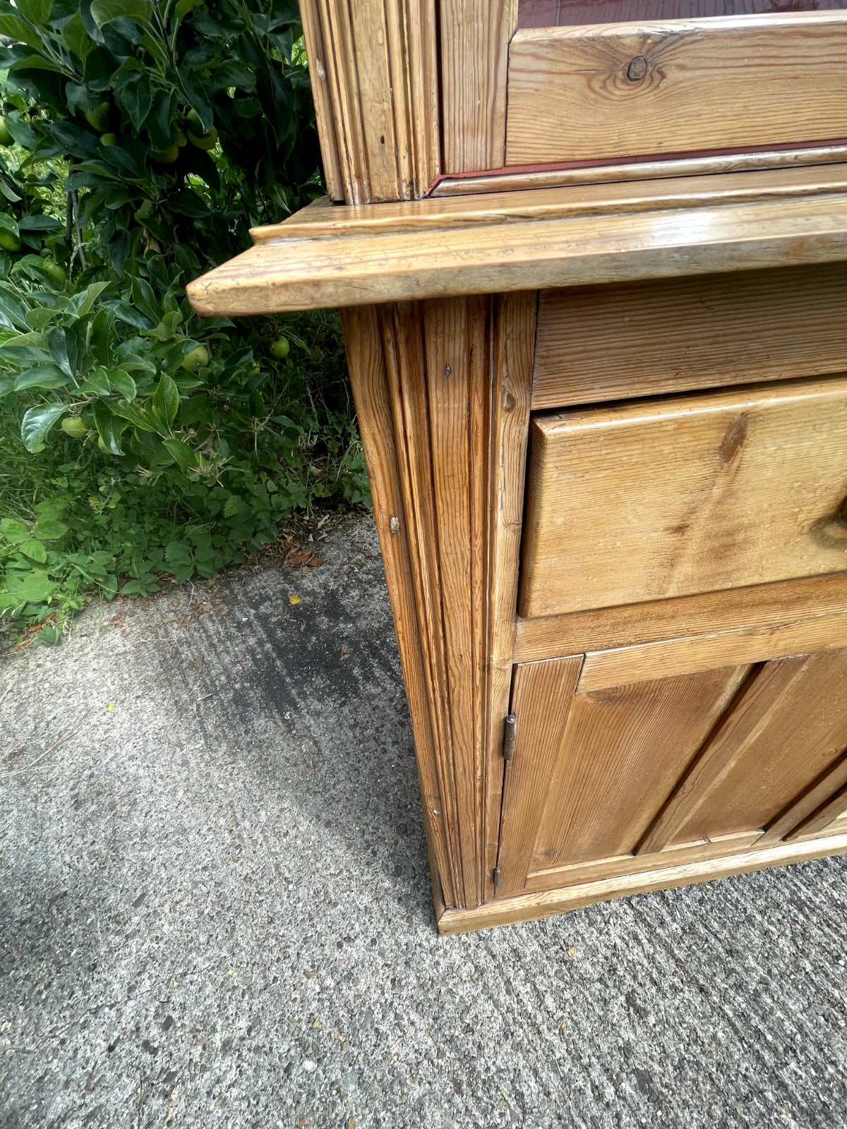 Wooden cabinet outdoors on a concrete surface with greenery in the background