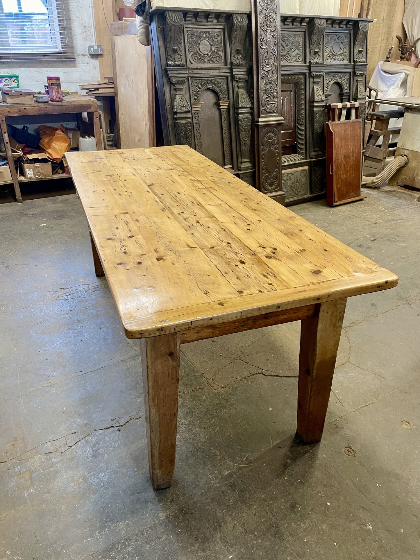 Large wooden table in a workshop setting with various items in the background