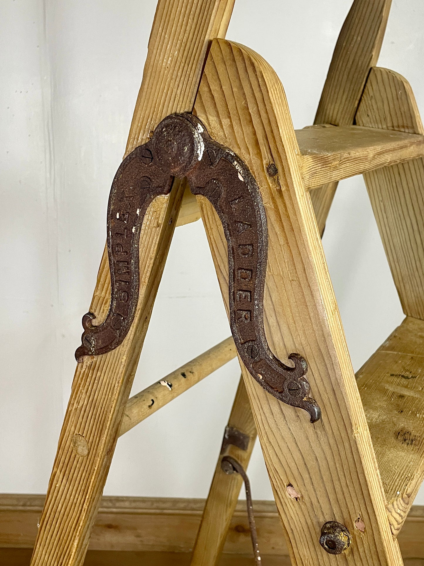 Wooden step ladder with a decorative metal hook on a white wall background
