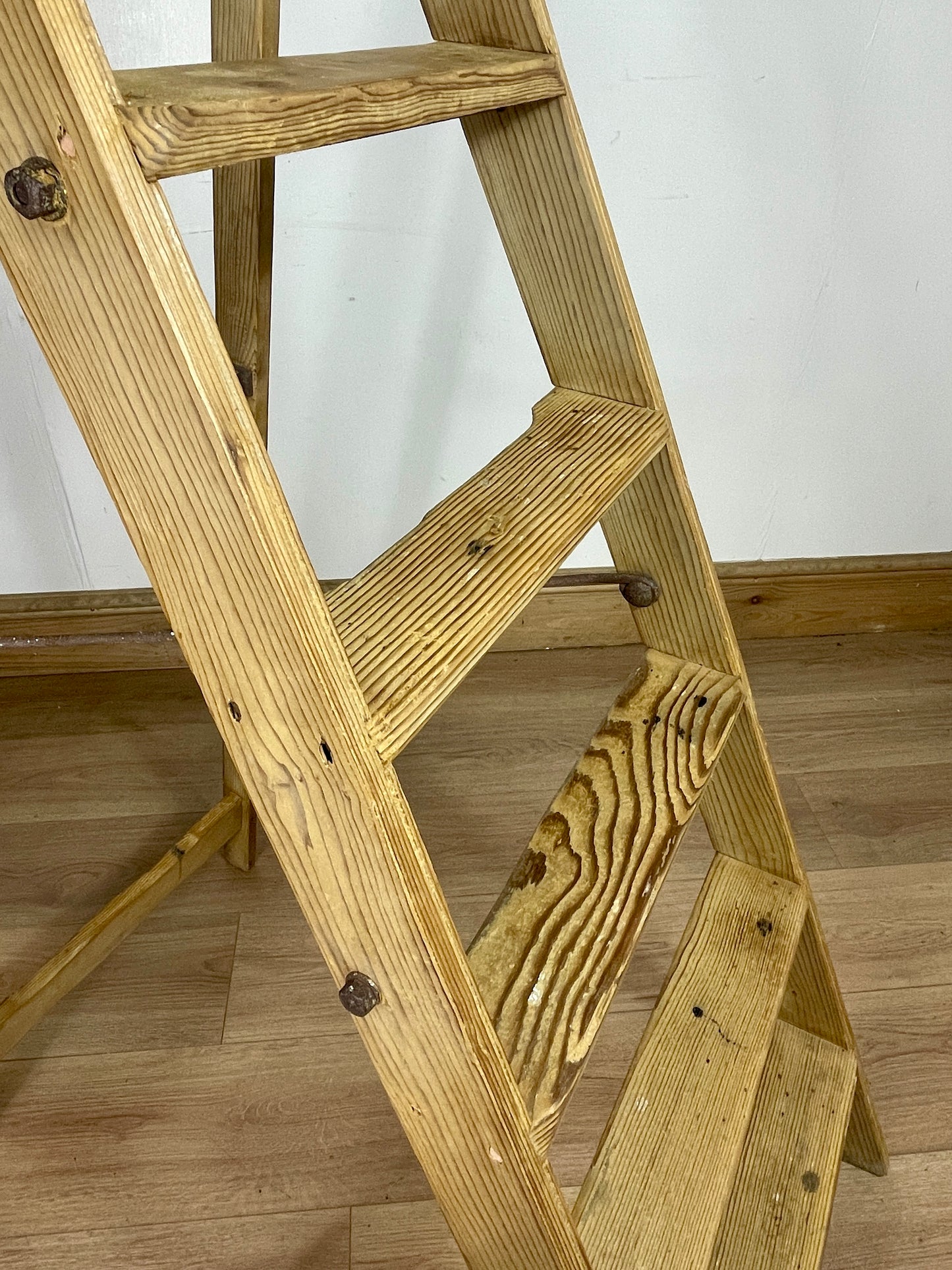 Wooden step ladder on a wooden floor with a white wall background