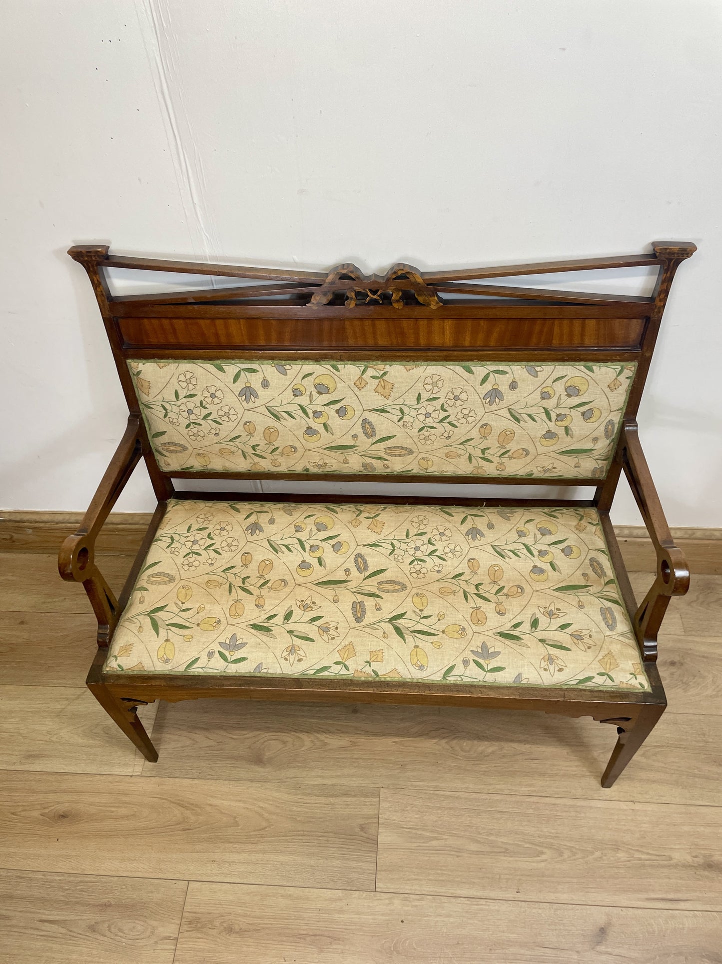 Wooden bench with floral-patterned cushion on a wooden floor against a white wall