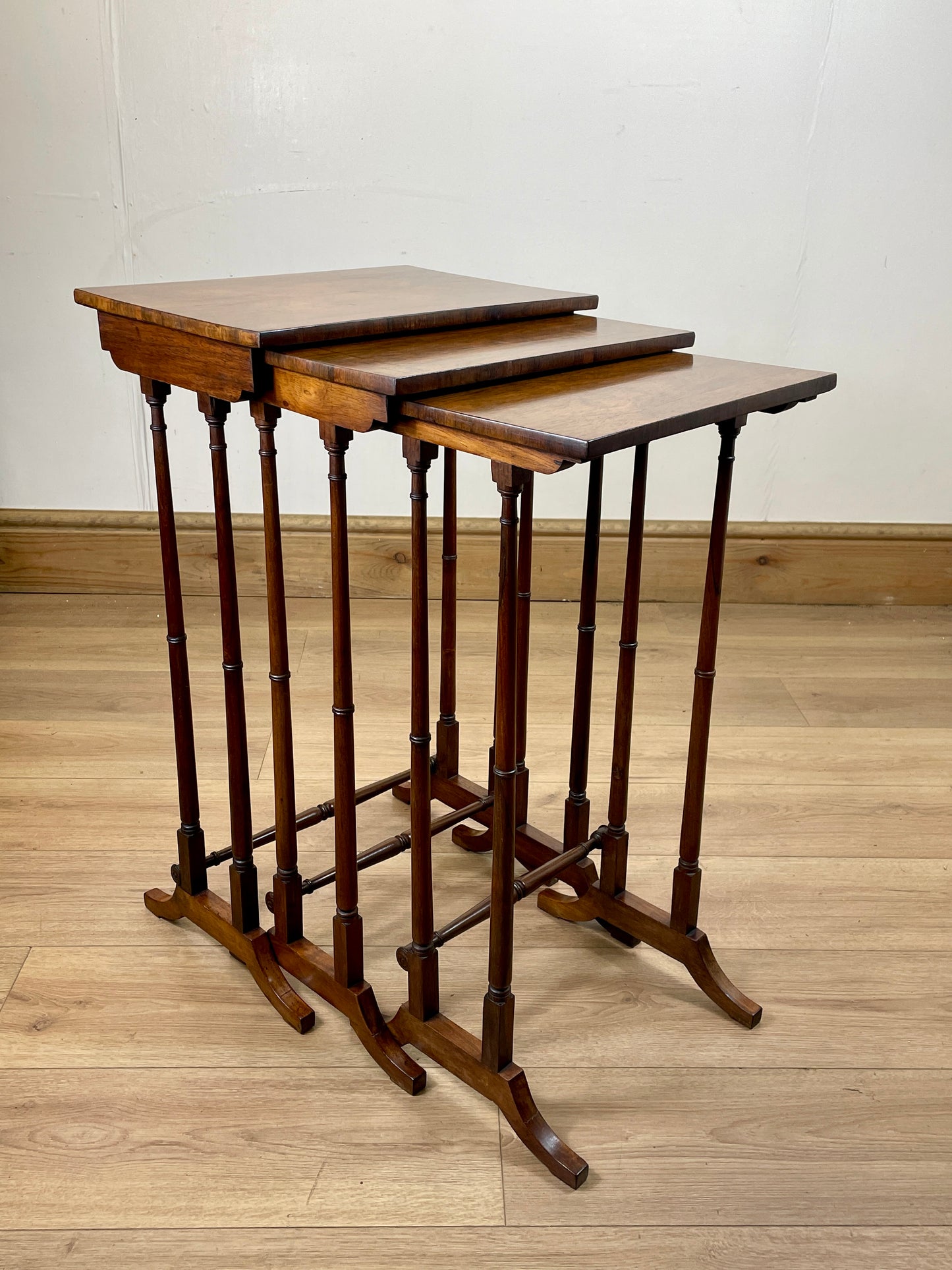 Set of three wooden nesting tables on a wooden floor with a white wall background