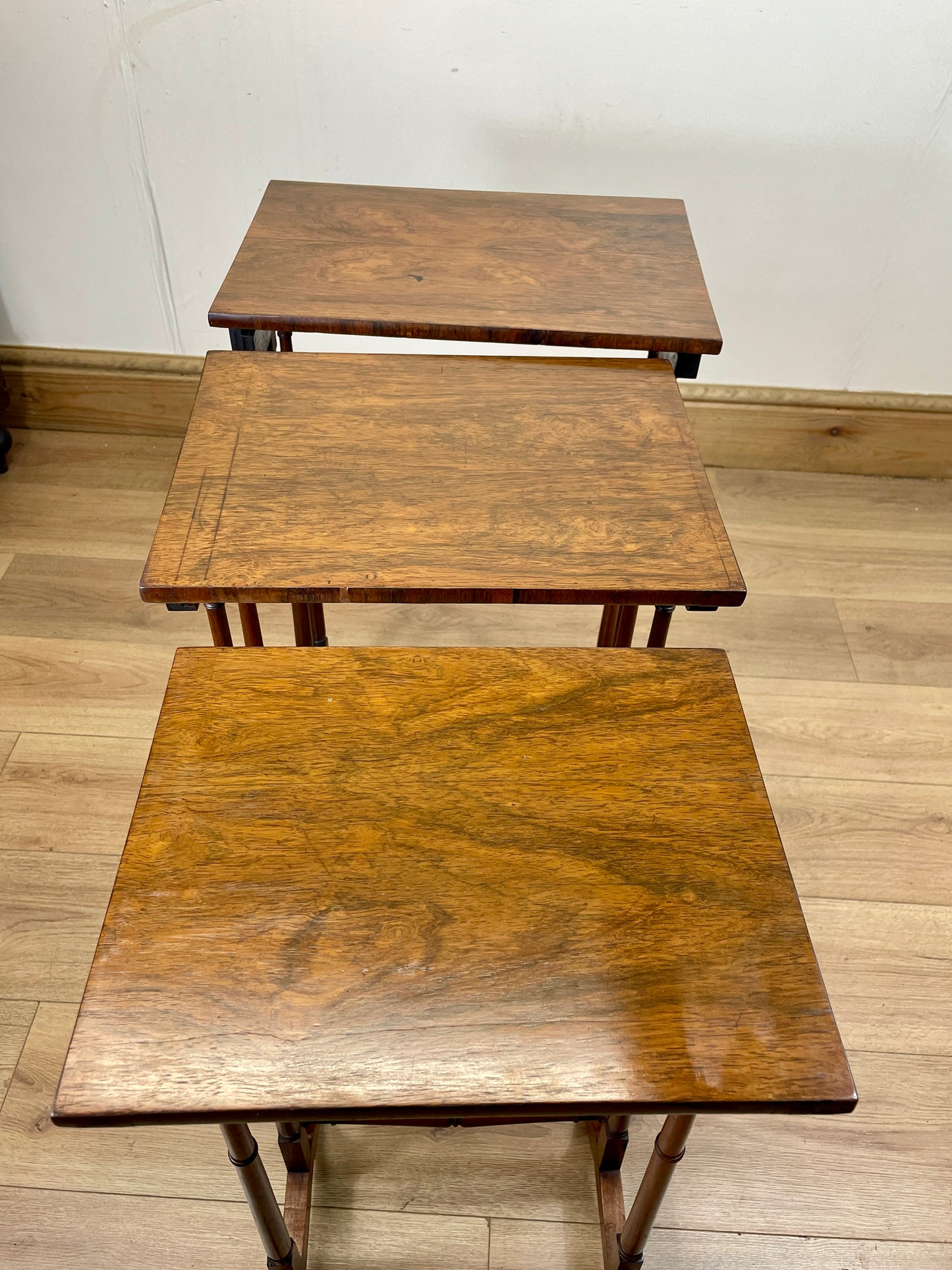 Three wooden nesting tables on a wooden floor with a white wall background