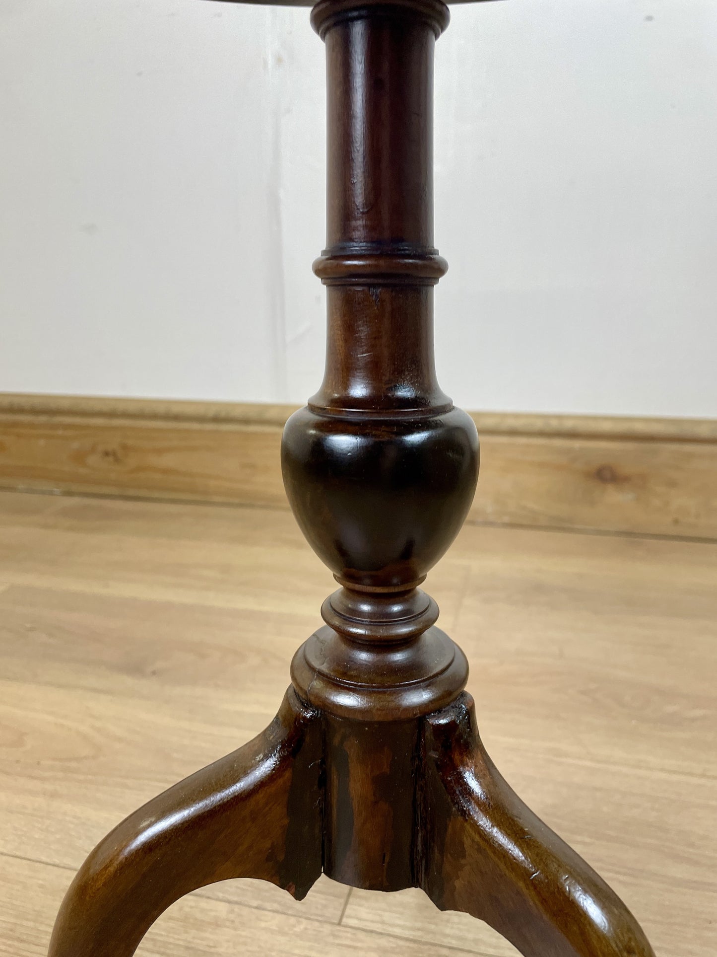 Wooden pedestal table base on a wooden floor with a white wall background