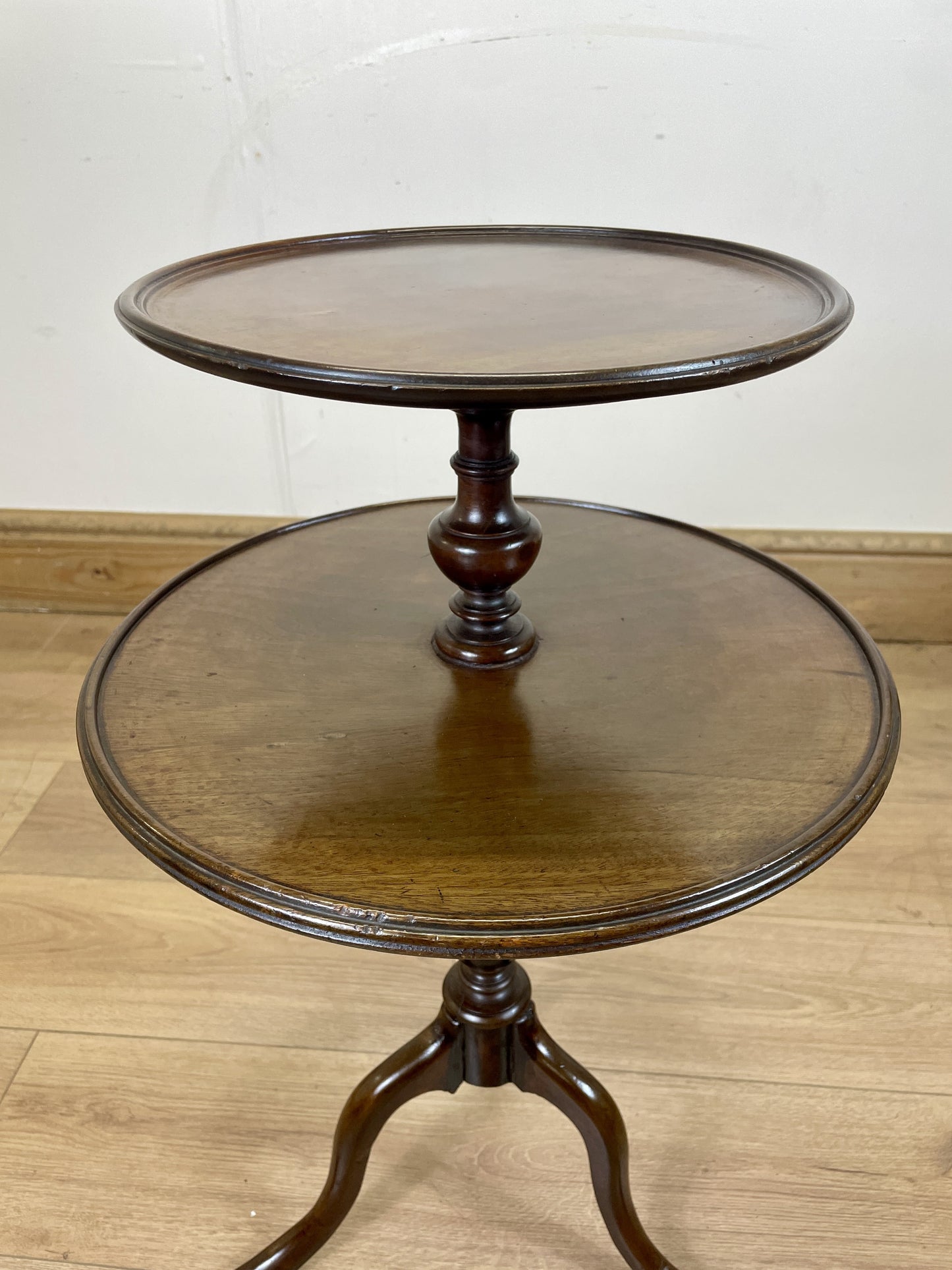Two-tiered wooden table on a wooden floor with a white wall background