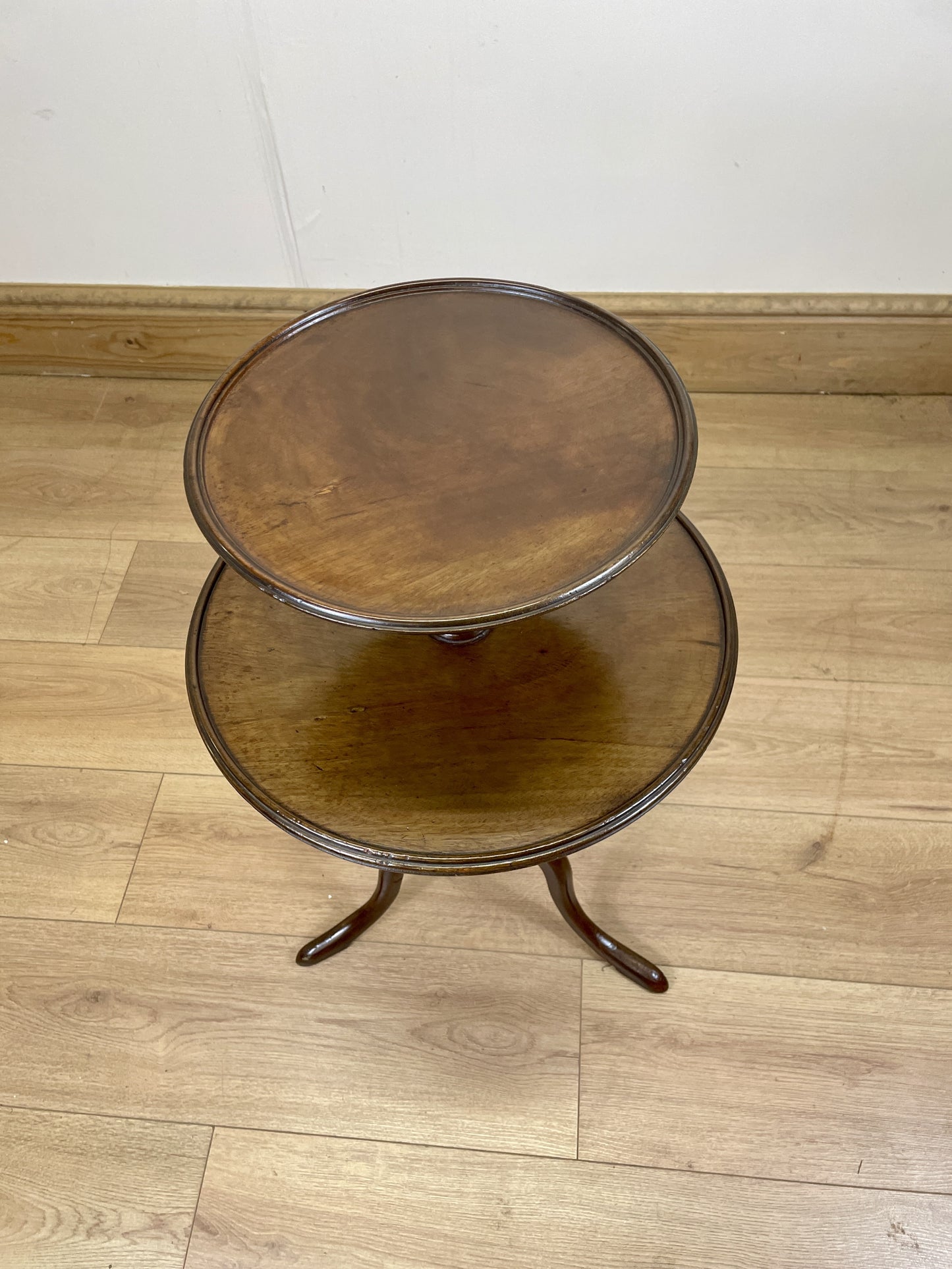 Two-tiered wooden side table on a wooden floor with a white wall background