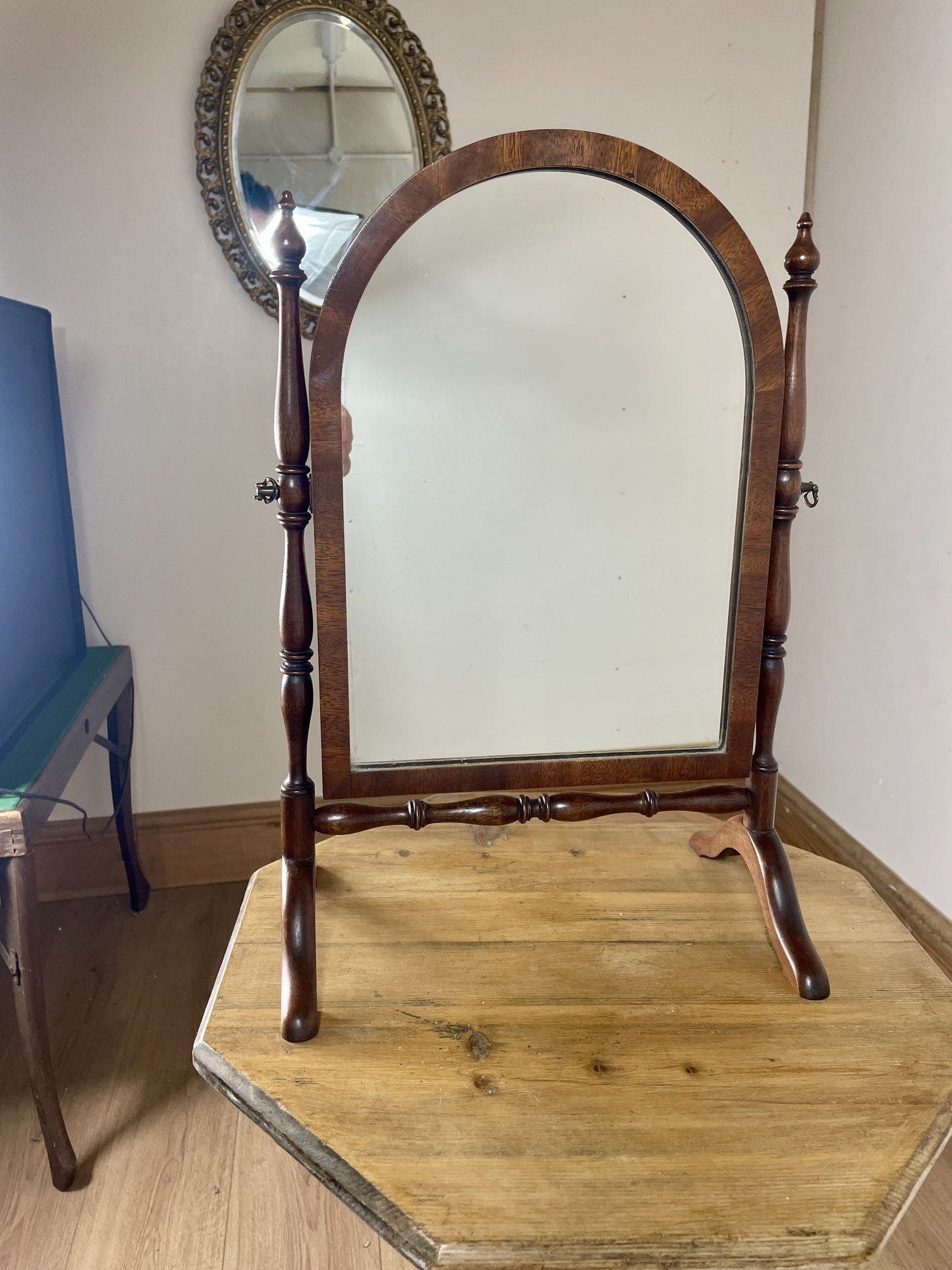 Wooden cheval mirror with decorative frame on a wooden platform against a white wall.