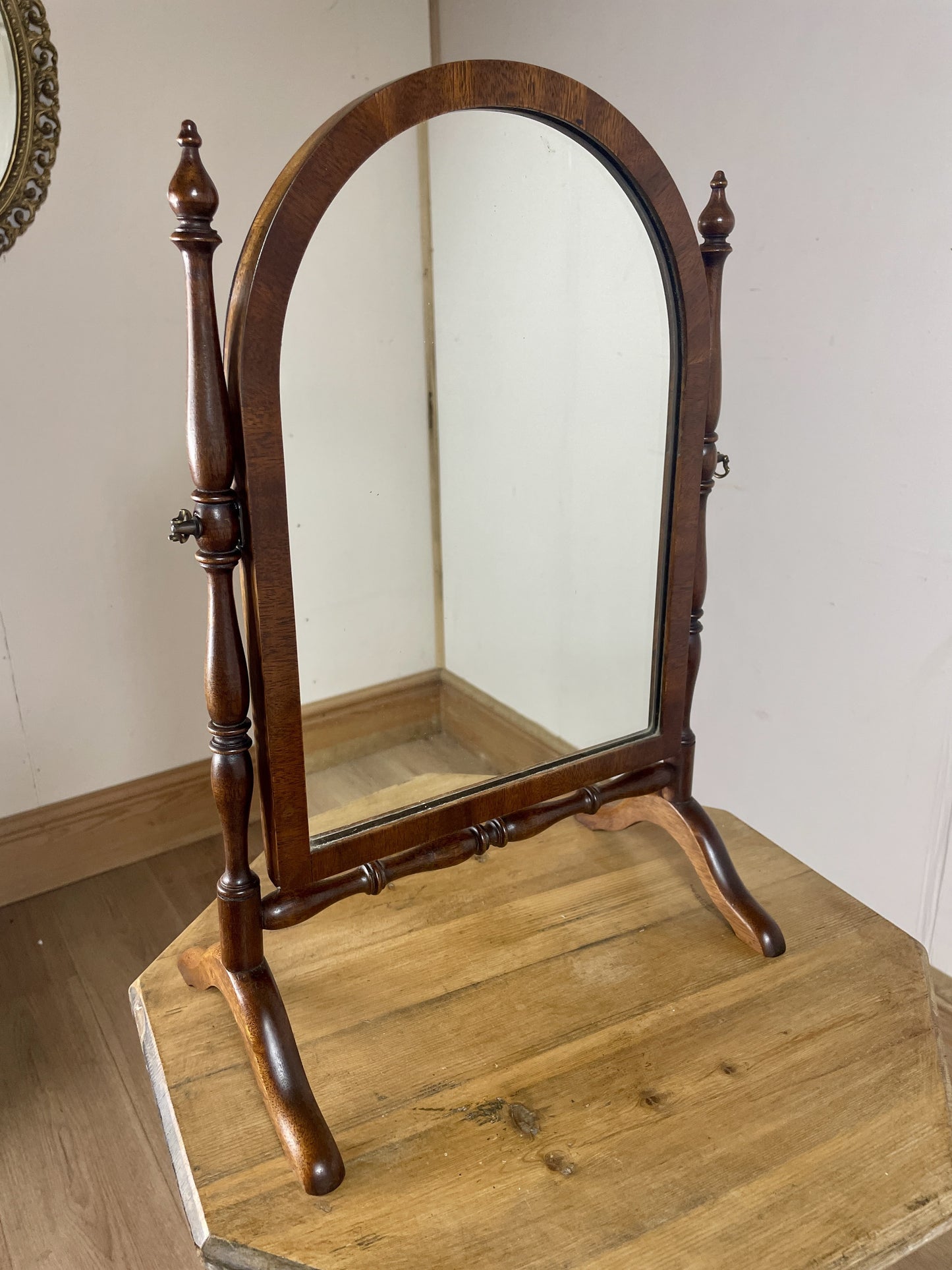 Wooden cheval mirror on a wooden floor with a plain wall background
