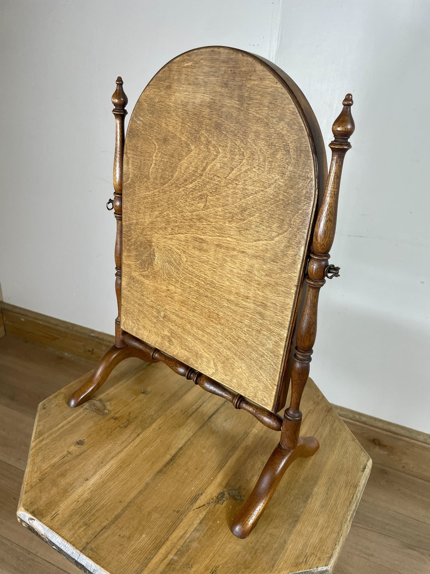 Wooden cheval mirror on a wooden stand against a white wall.
