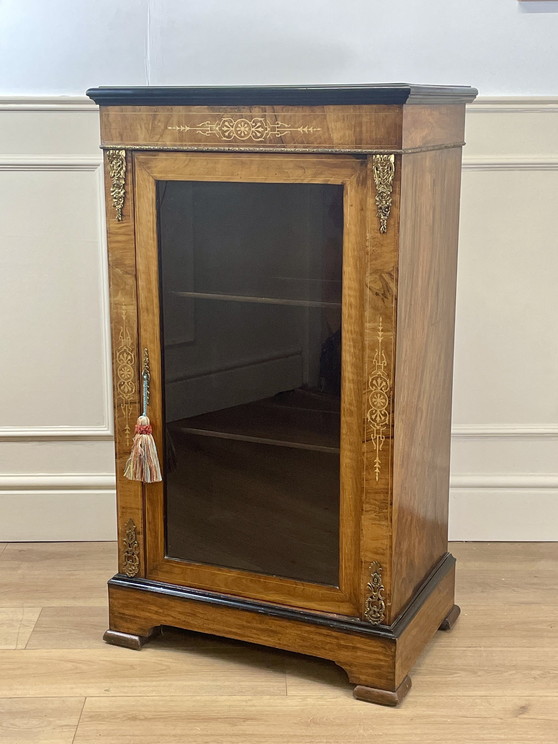 Wooden display cabinet with glass door on a wooden floor against a white wall.