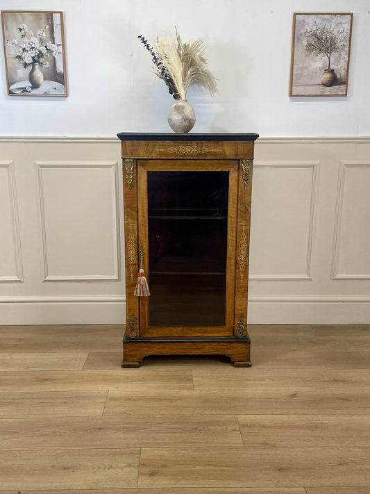 Wooden cabinet with a glass front on a wooden floor against a white wall.